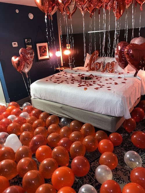 Bedroom decorated with heart balloons and rose petals on the bed