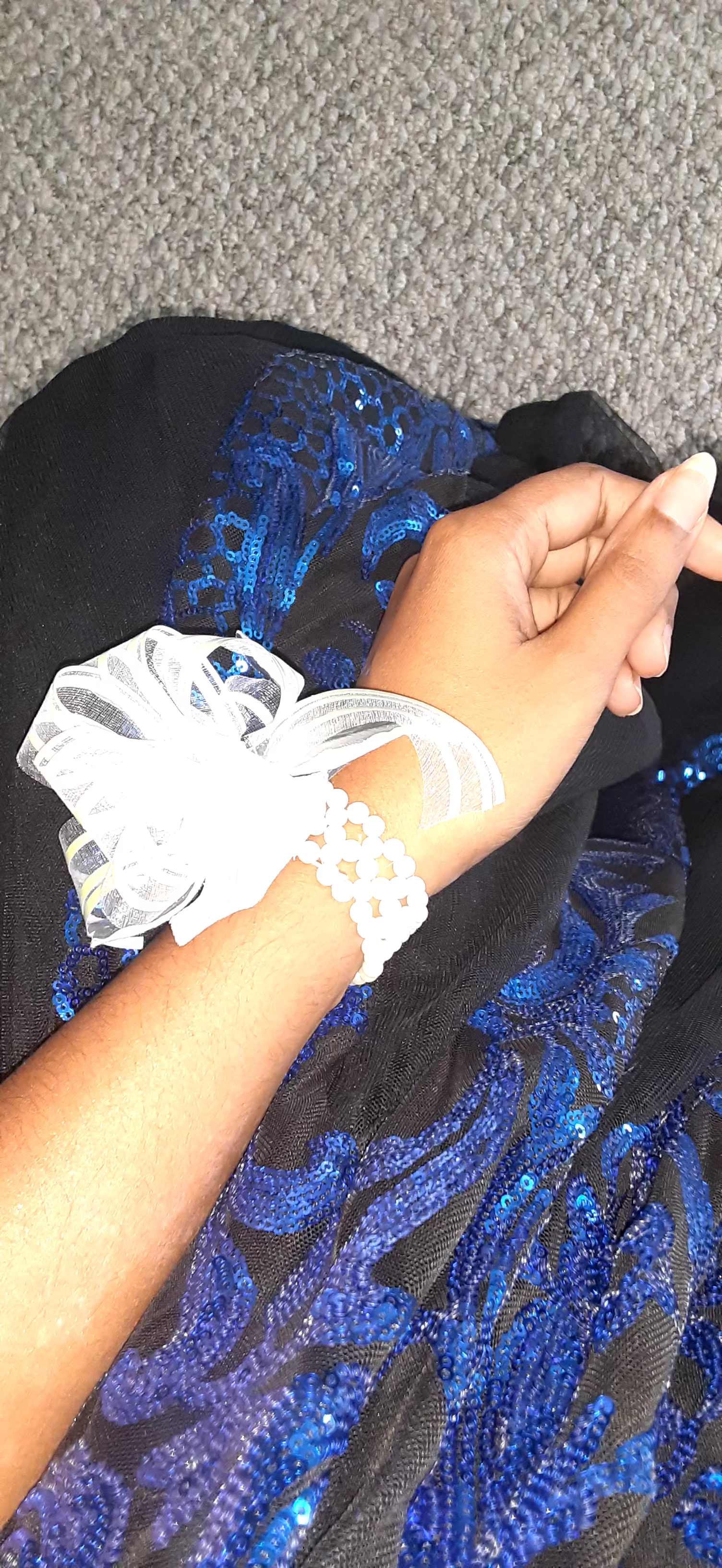 Hand wearing a white ribbon bracelet over black and blue sequined fabric