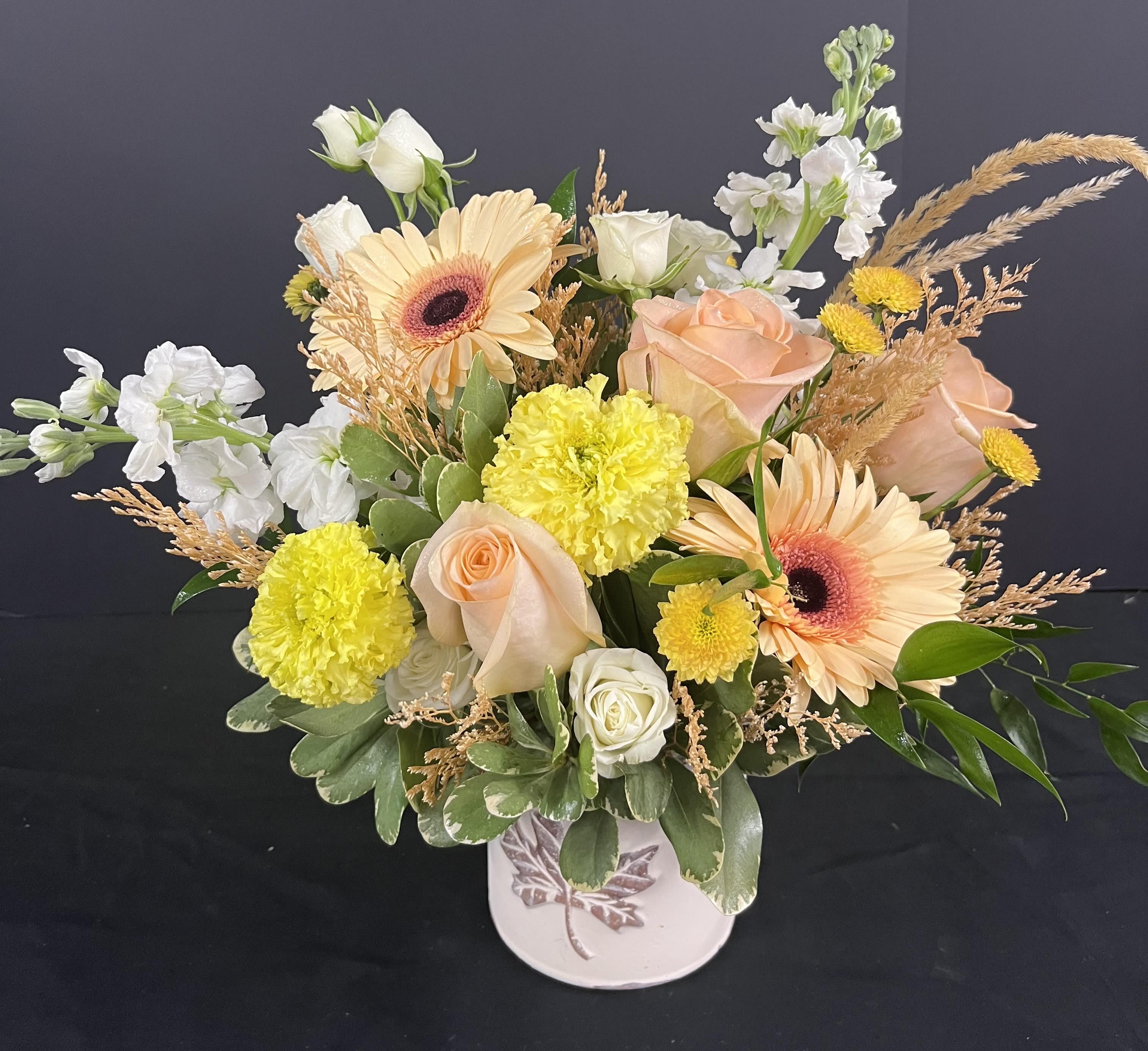 Mixed bouquet of peach roses, gerbera daisies, and yellow carnations in a white vase