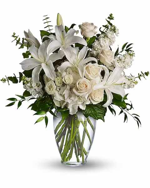 White lilies, roses, and hydrangeas arranged in a clear glass vase.