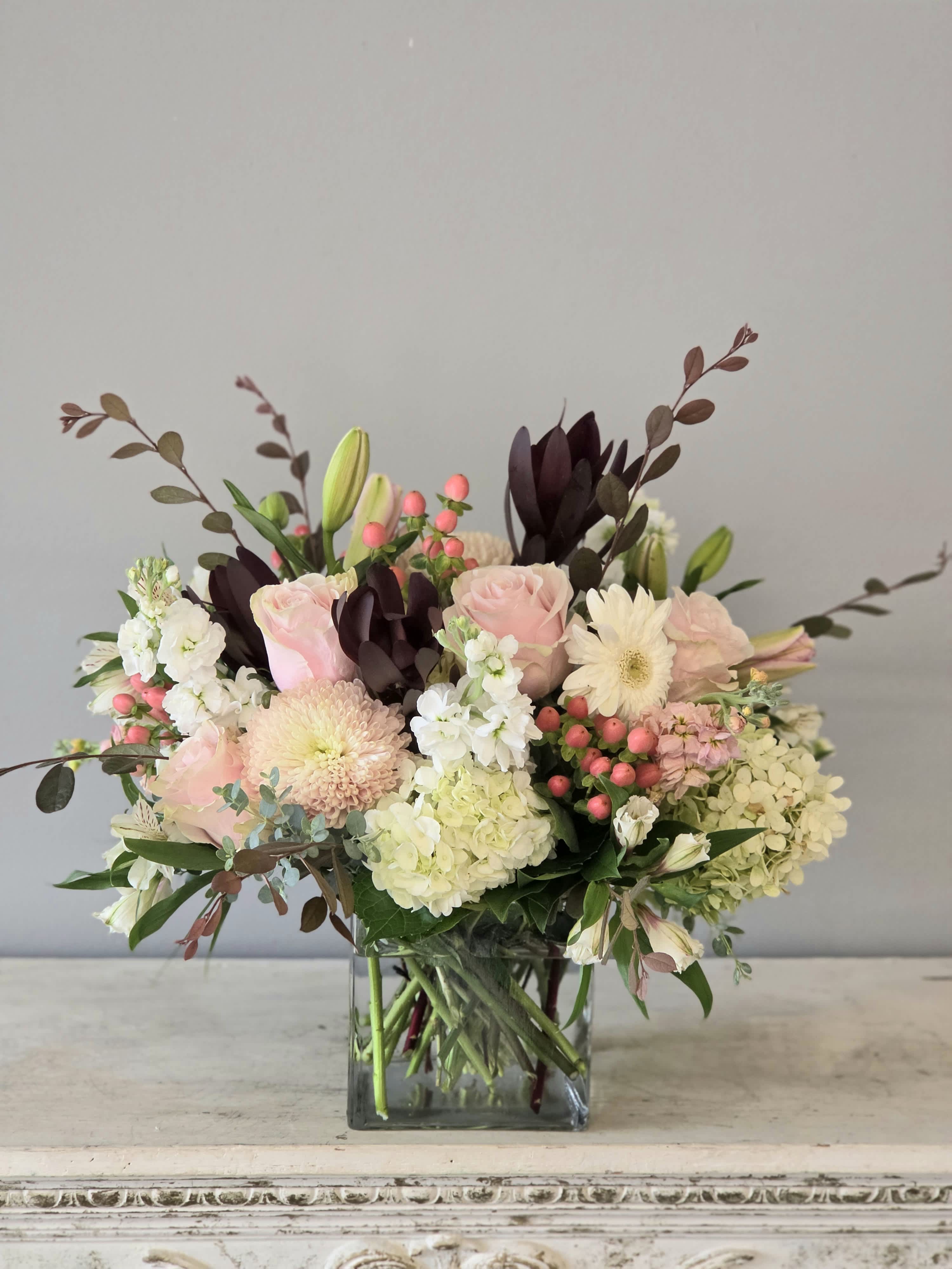 Pink roses and white blooms arranged in a square glass vase