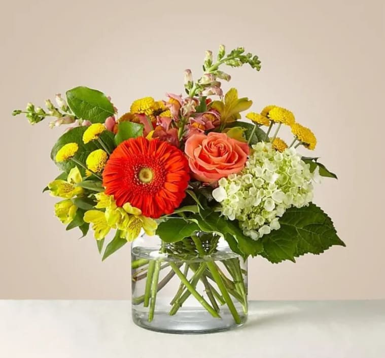 Mixed bouquet with a coral rose, red gerbera daisy, and yellow flowers in a glass vase