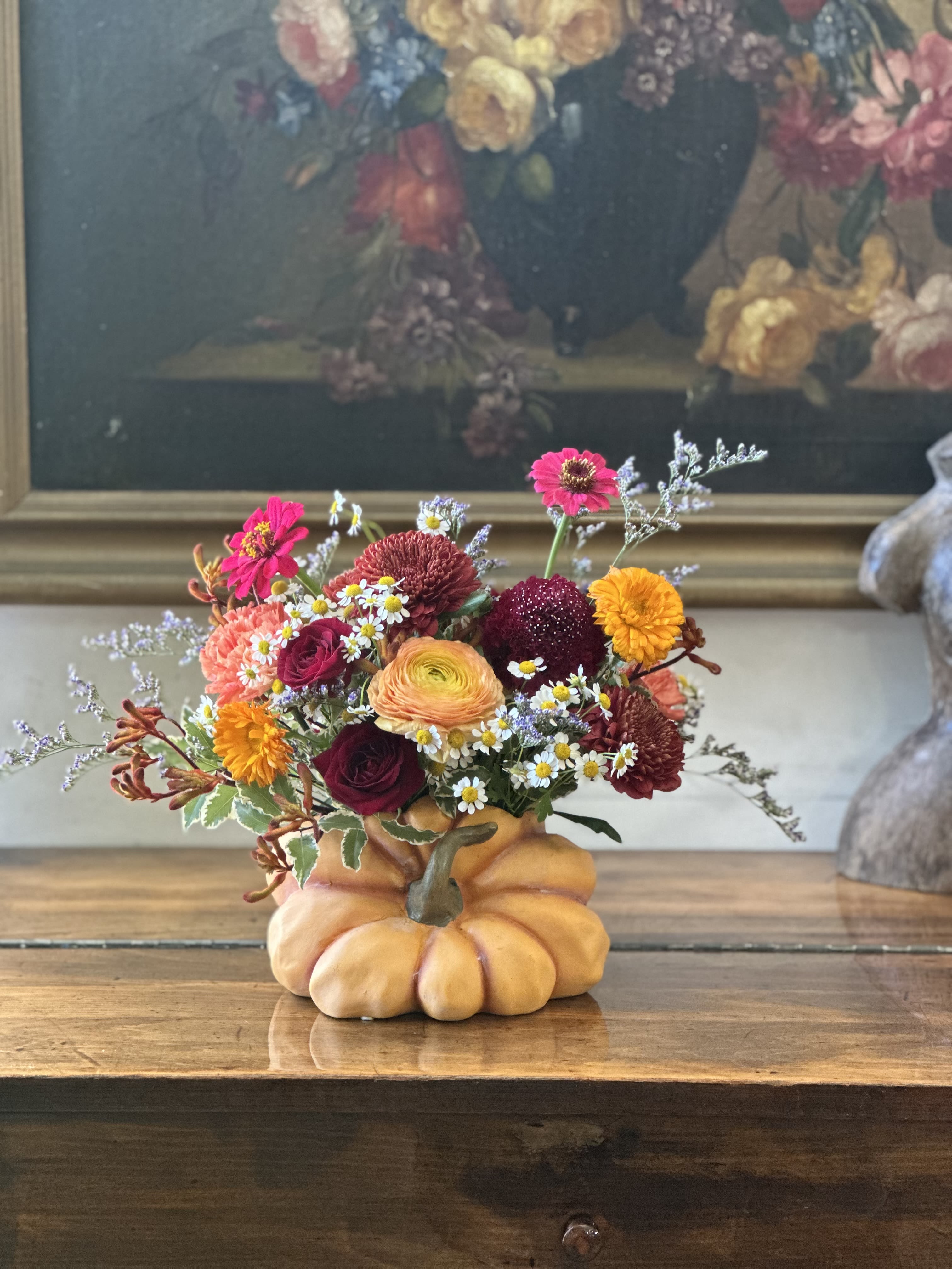 Autumn-toned flower arrangement in a pumpkin-shaped container on a wooden table
