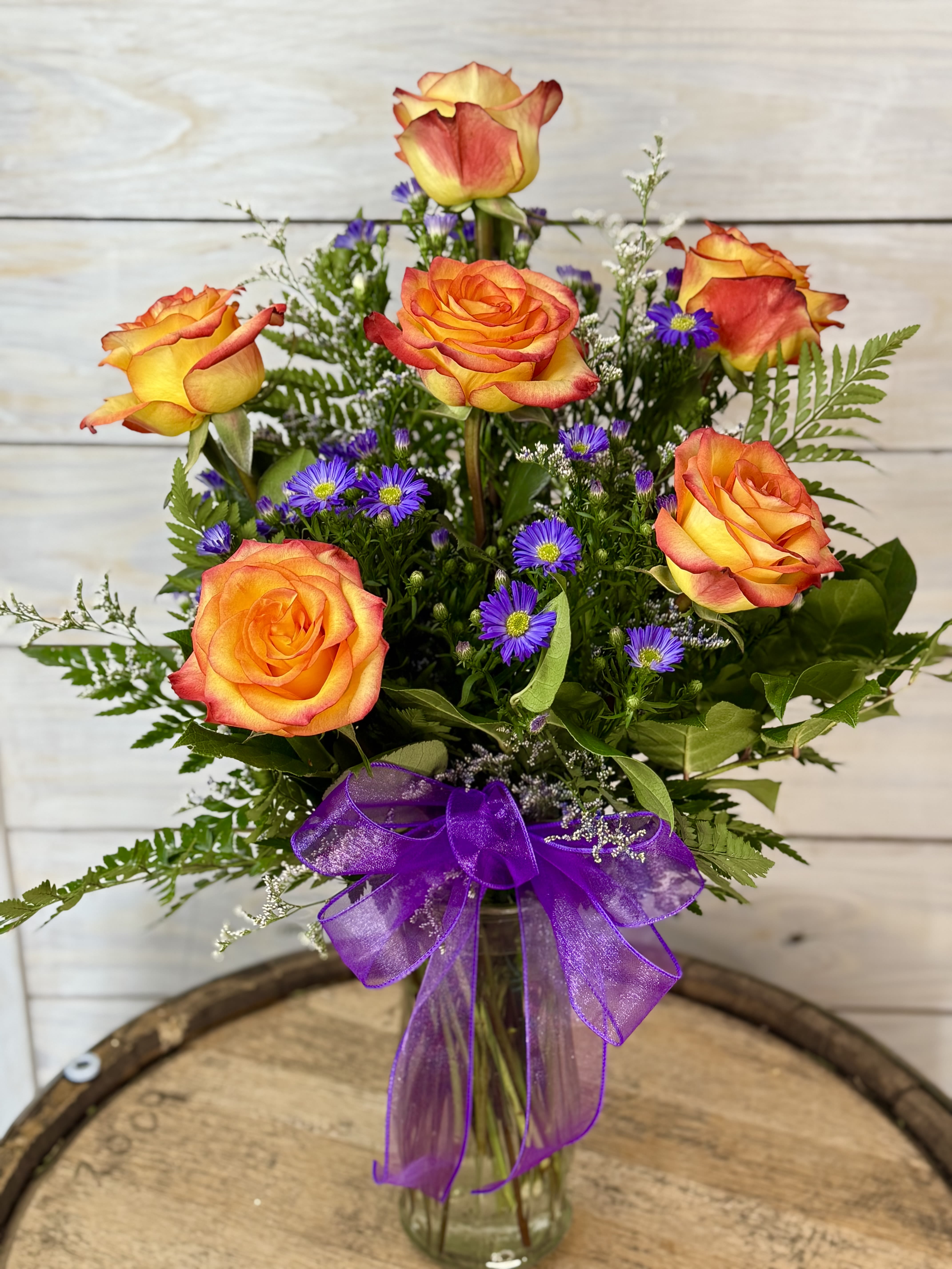 Bouquet of orange-yellow roses with purple daisies in a glass vase