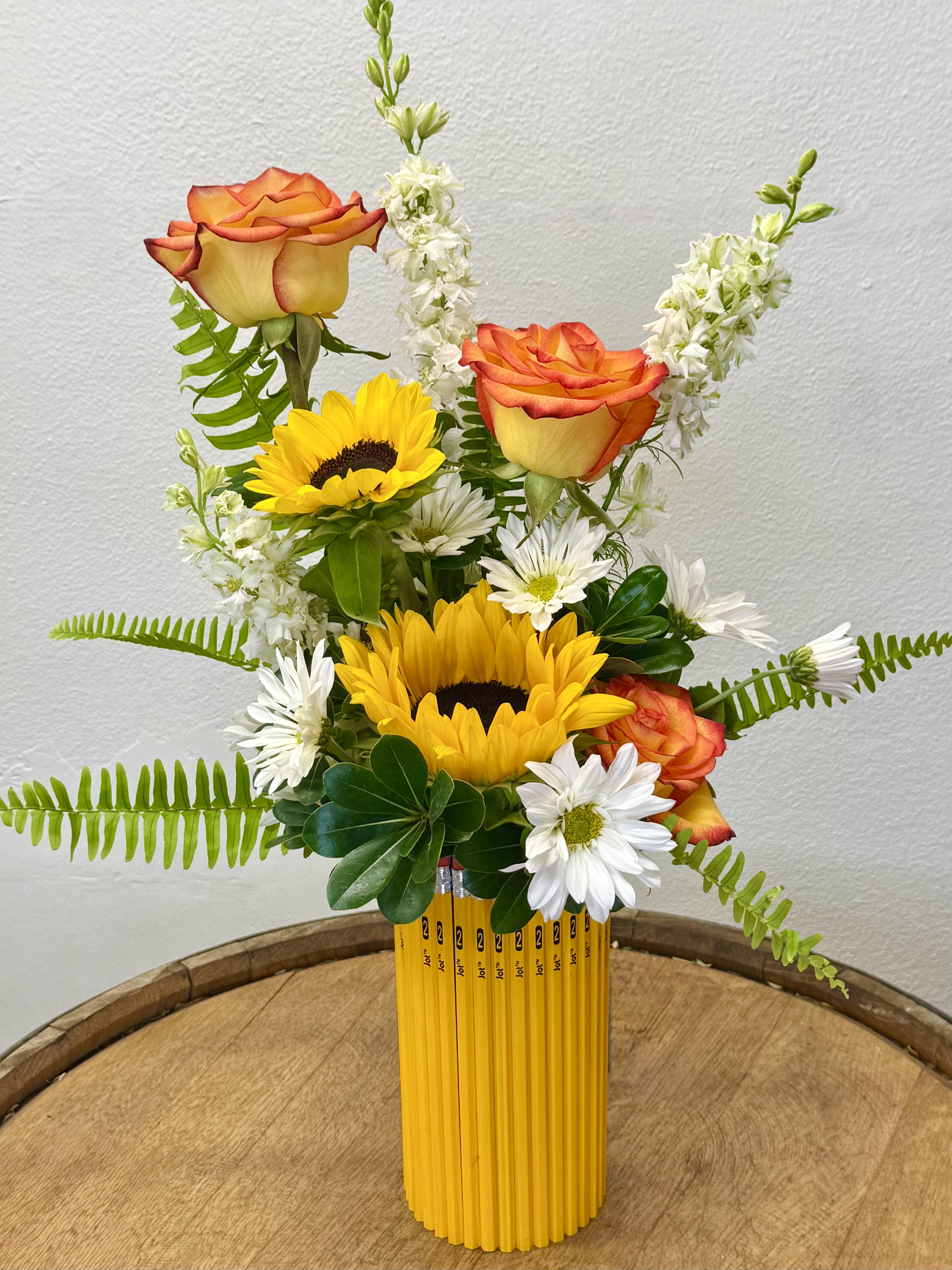 Sunflowers, orange roses, and white daisies in a yellow pencil vase