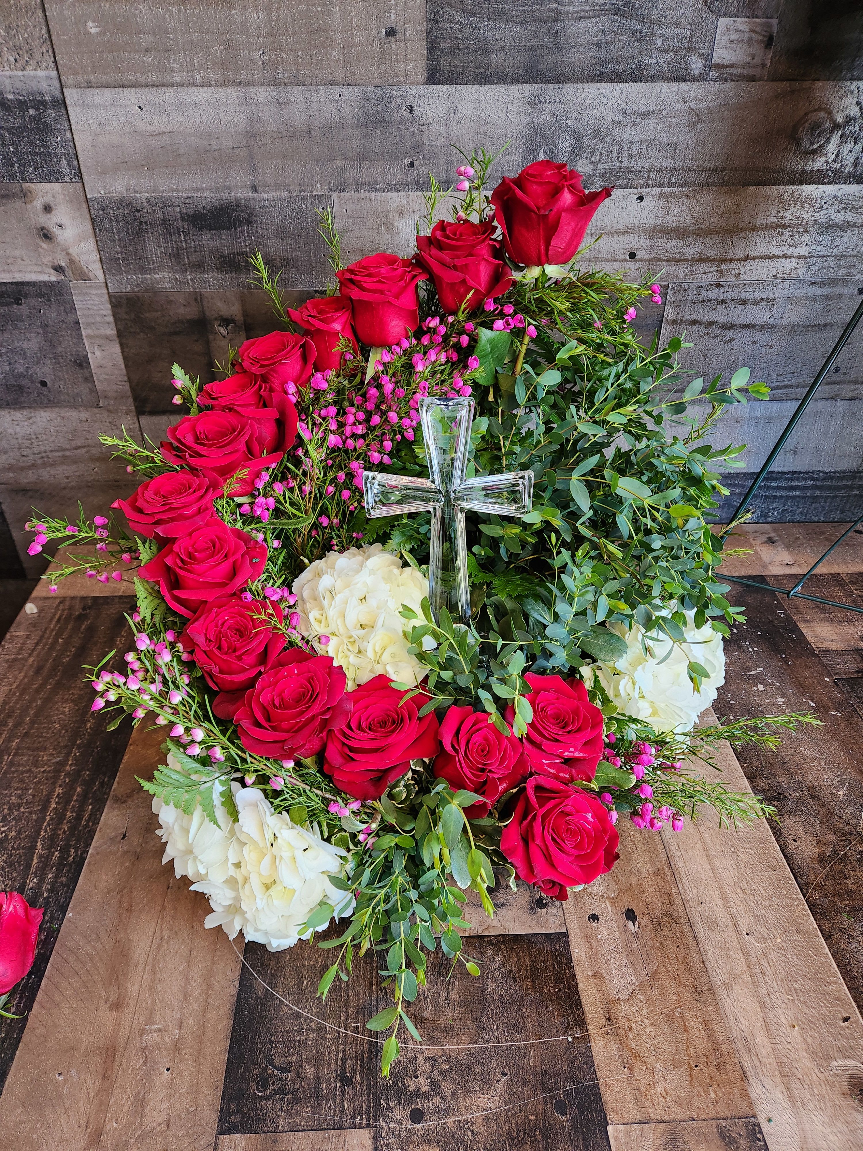 Circular wreath of red roses and white hydrangeas with a clear glass cross in the center