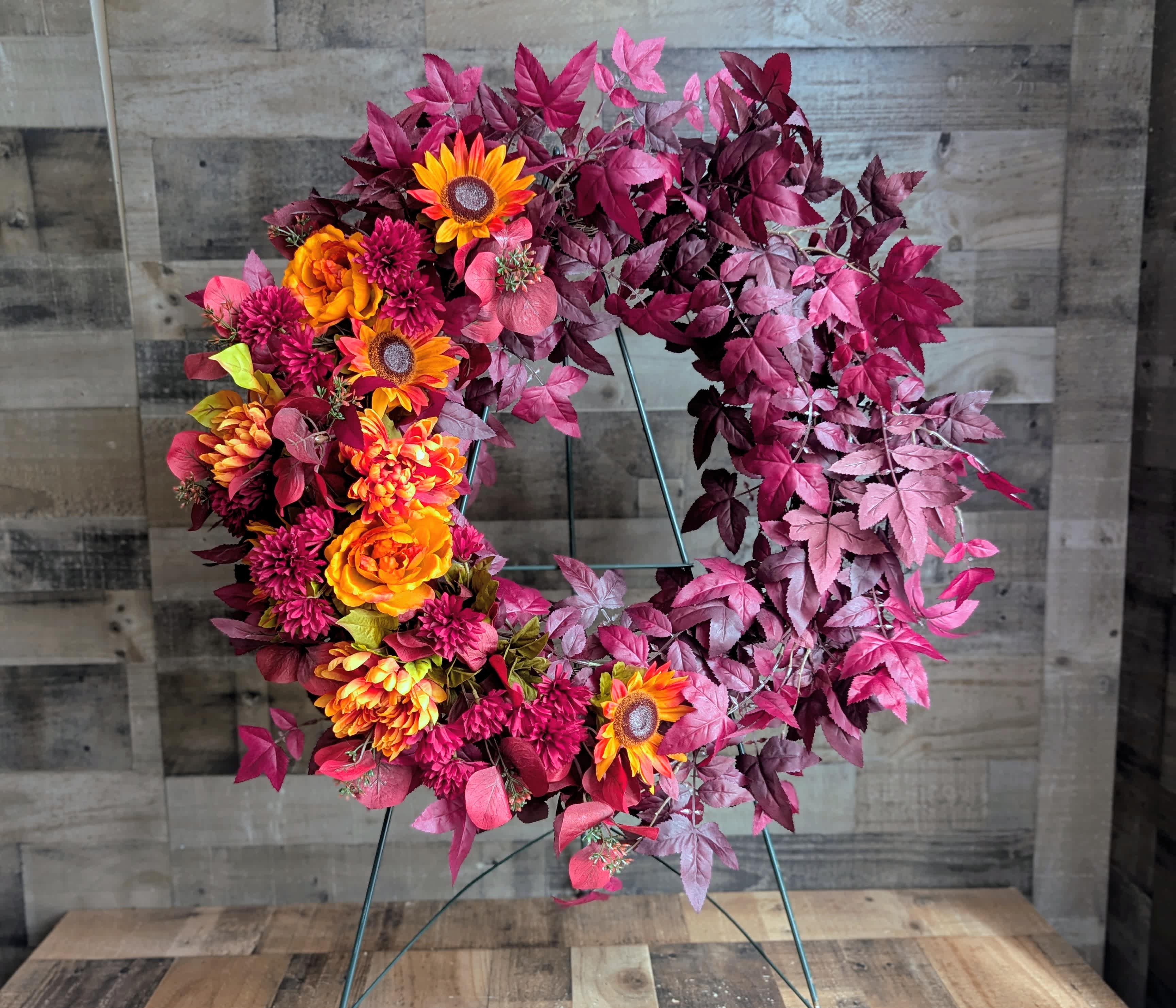 Circular wreath with orange and magenta flowers on a metal stand