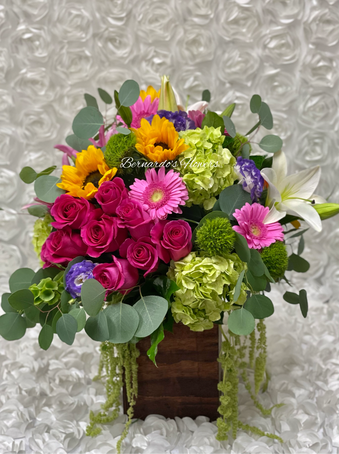 Mixed bouquet with pink roses, sunflowers, lilies, and green hydrangeas in a wooden box