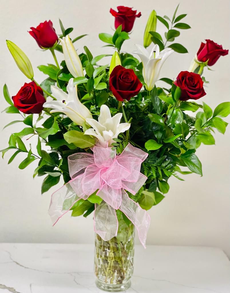 Red roses and white lilies in a clear glass vase with a pink bow