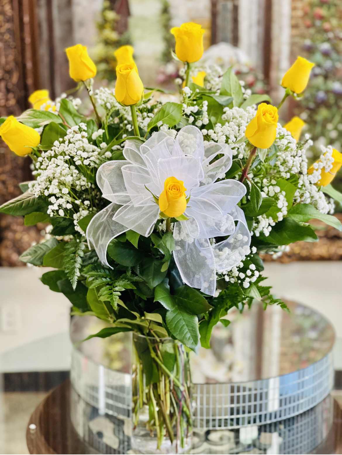 Yellow roses arranged in a clear glass vase with white ribbon