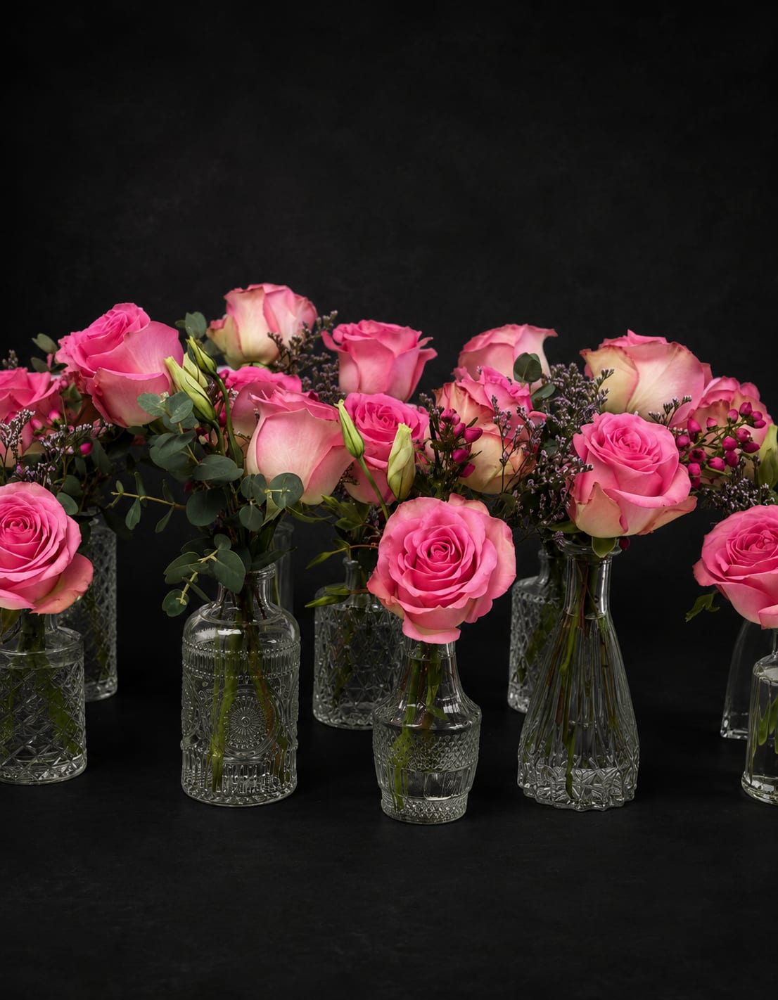 Pink roses arranged in small clear glass vases with greenery