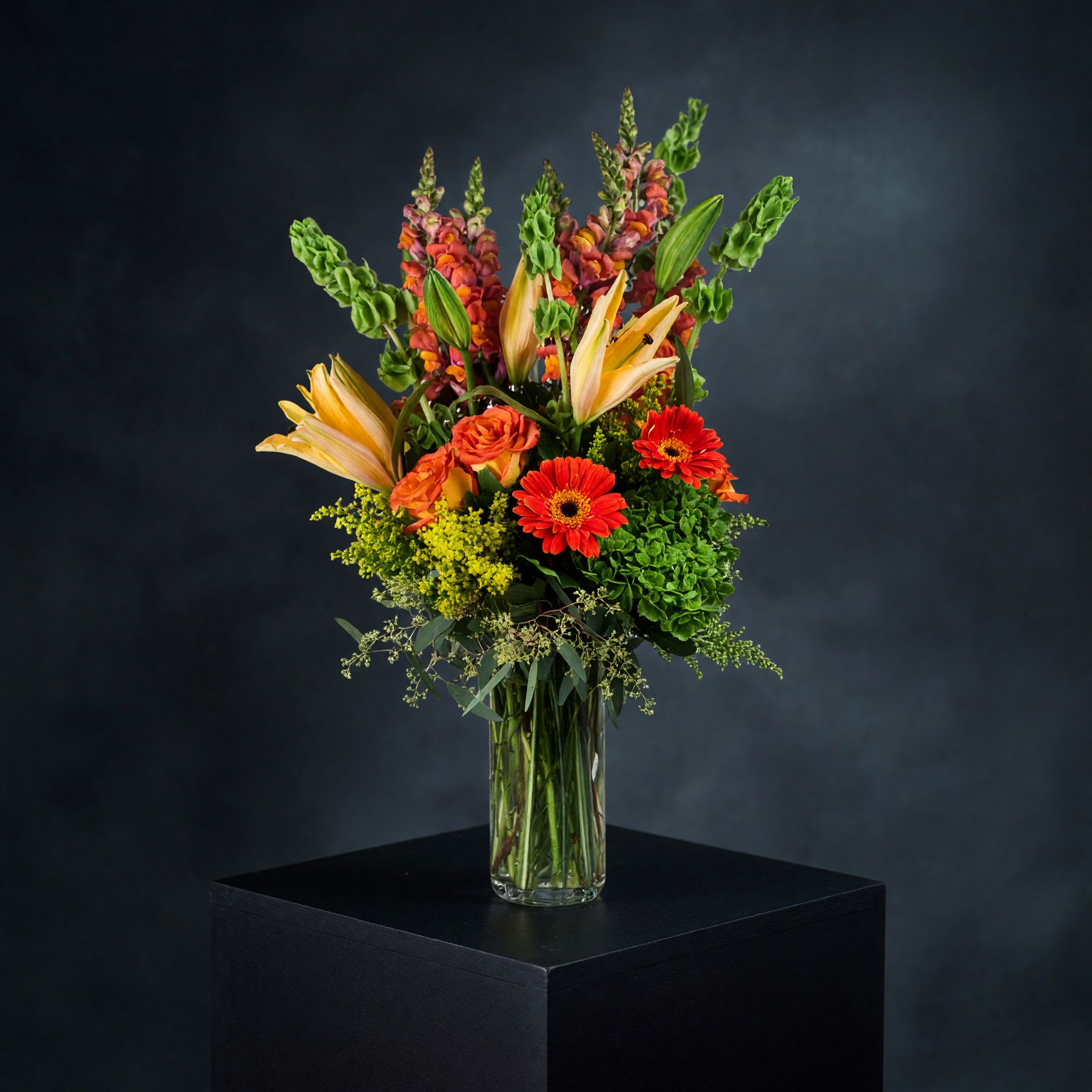 Buenos Dias  - Rise and shine with this tall and bright arrangement. Tall reaching daisies, bells of Ireland and lilies in bright orange and green make this arrangement pop. Perfect for Cinco De Mayo, wishing somebody a happy birthday or welcoming a new baby.   APPROXIMATE DIMENSIONS 16" W X 31" H
