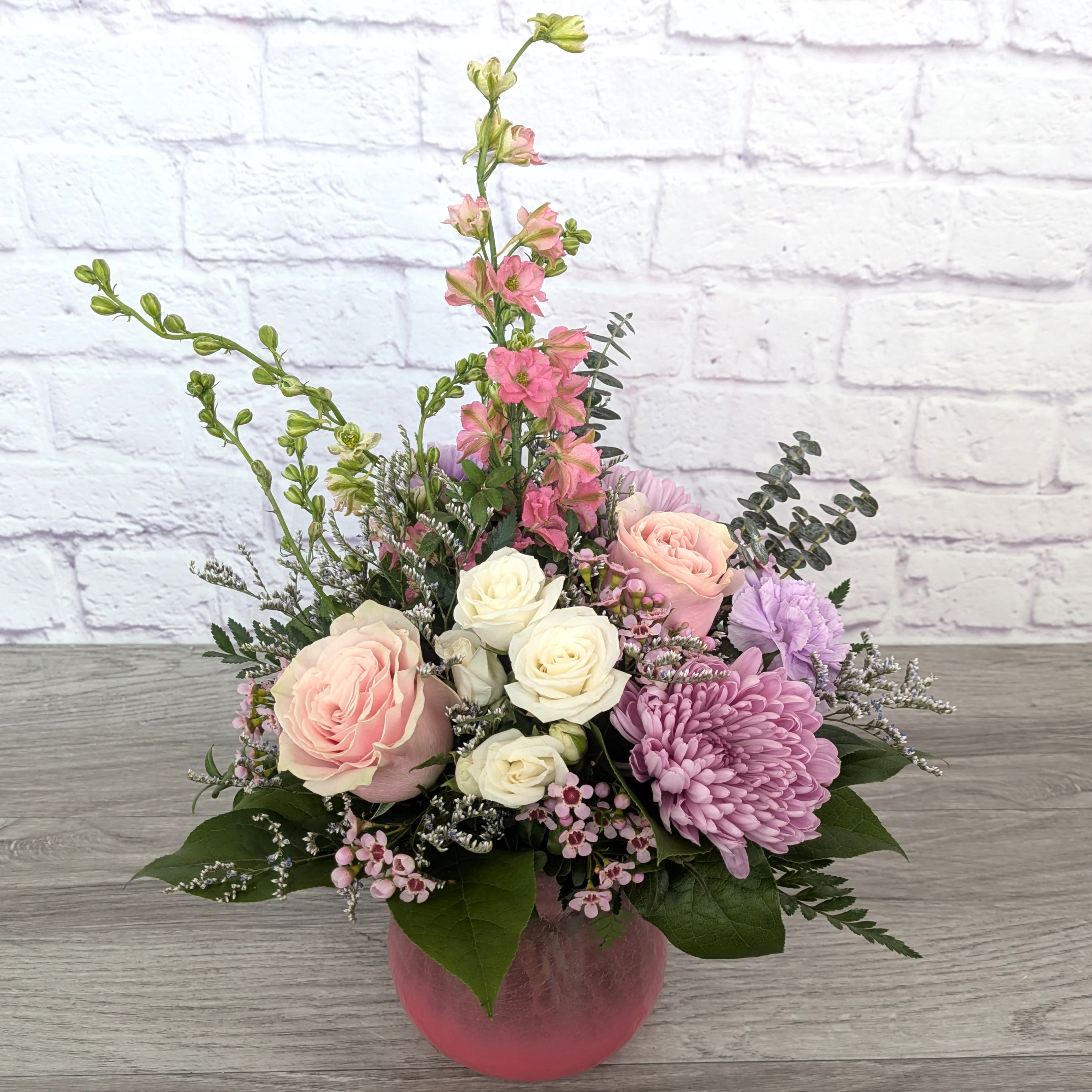 Pink and white roses with purple blooms in a pink vase