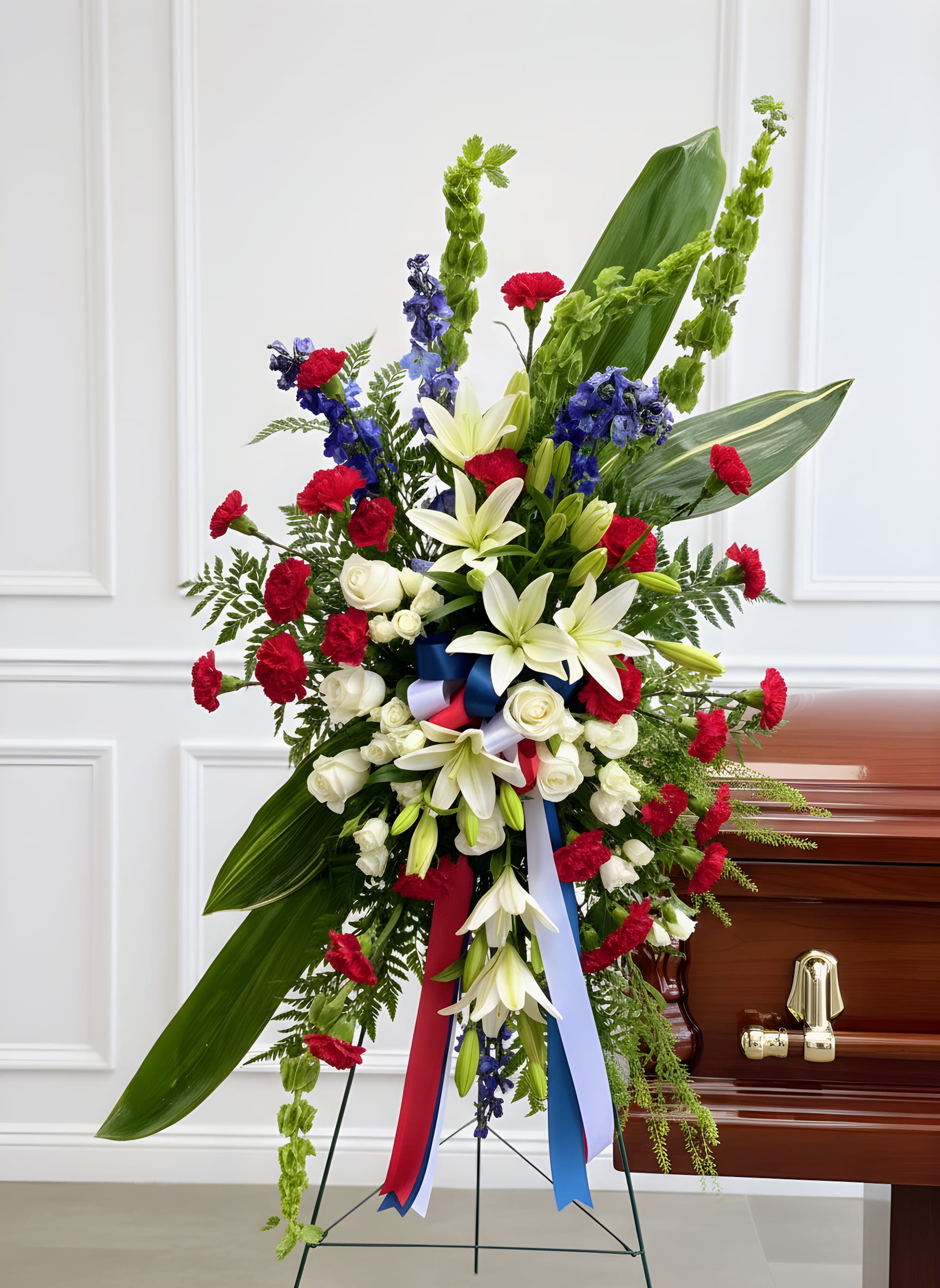 Standing funeral spray with white lilies, red carnations, and blue flowers
