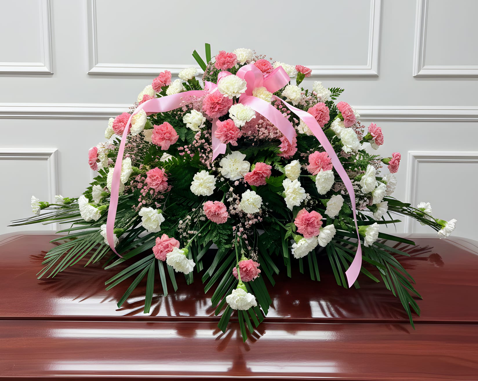 Pink and white carnation spray with a pink ribbon on a casket