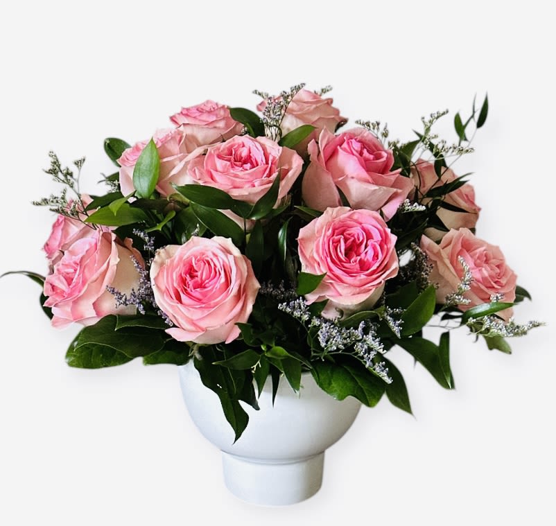 Pink roses arranged in a white vase with greenery