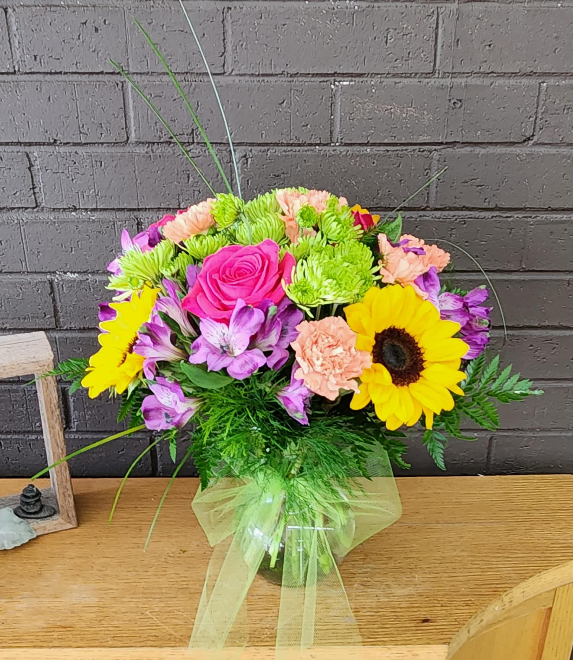Mixed bouquet with pink roses, sunflowers, and purple flowers in a glass vase
