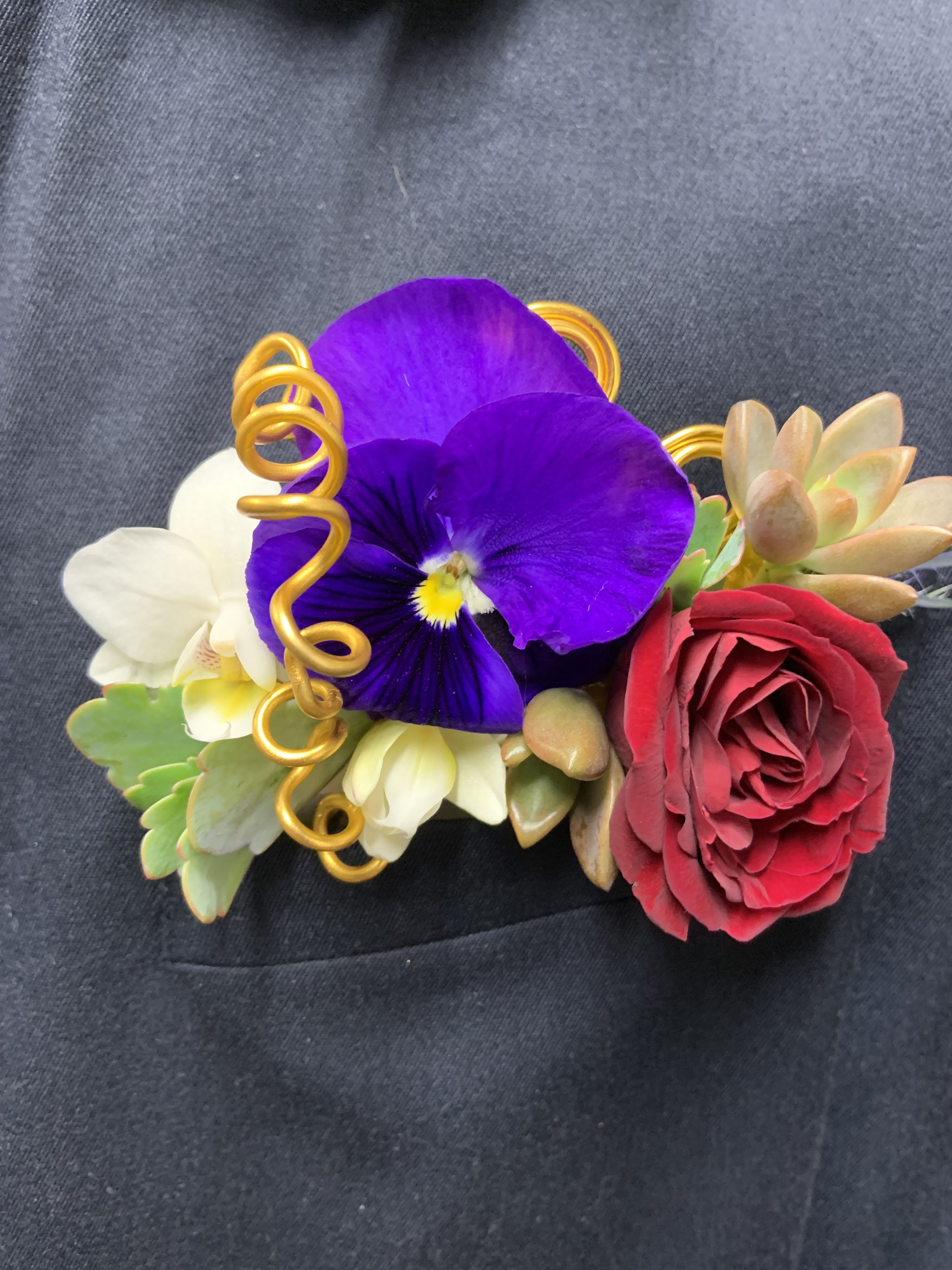 Floral wrist corsage with purple pansy, red rose, and succulents