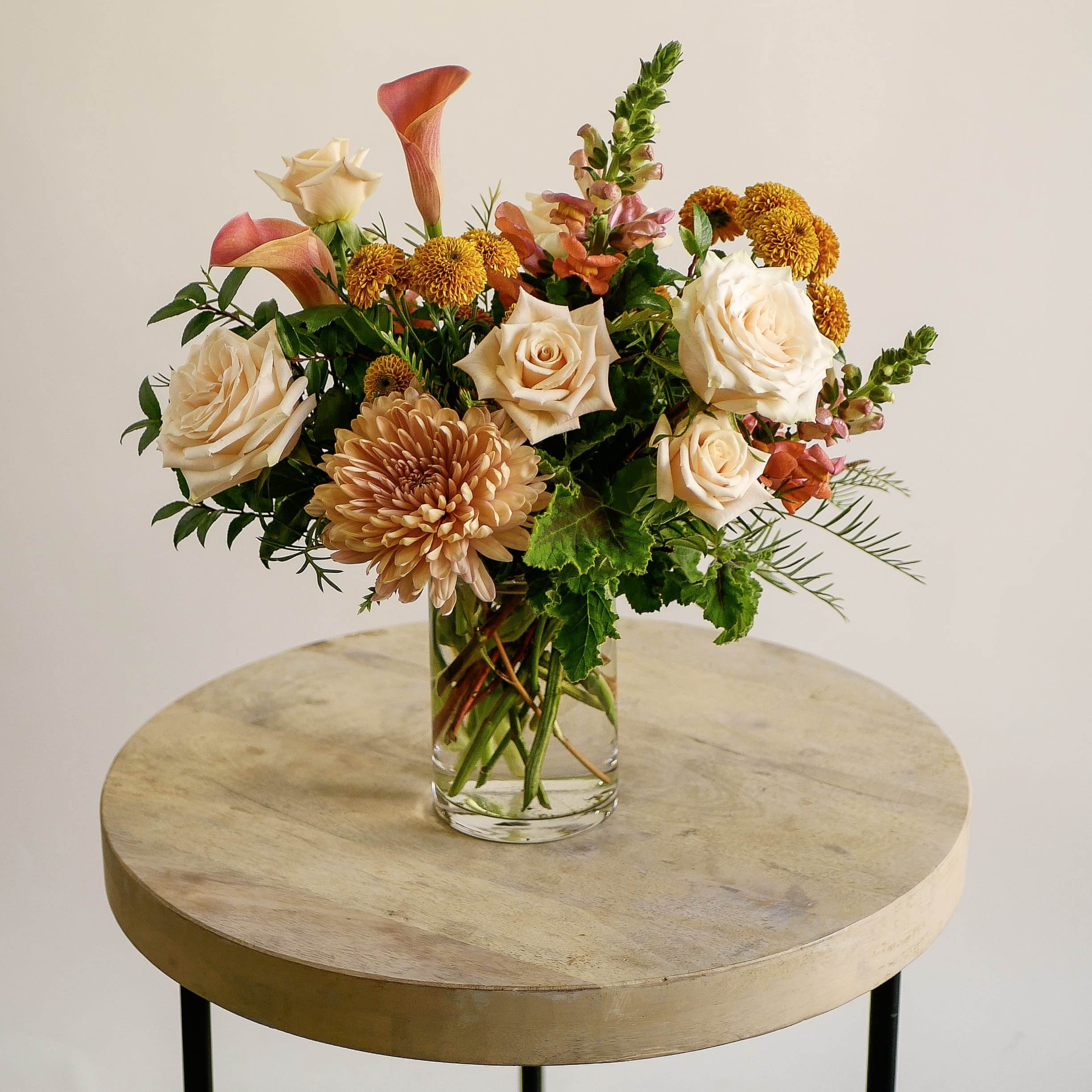 Wild Solstice - Soft, warm, and effortlessly elegant — Wild Solstice embodies the beauty of California’s early fall light. Featuring peach and cream roses, coral calla lilies, bronze mums, and golden accents, this lush arrangement celebrates the gentle transition of seasons with modern refinement. Arranged in a clear glass vase with airy, organic movement, Wild Solstice is perfect for Thanksgiving gatherings, birthday celebrations, or as a seasonal centerpiece for your home. Its blend of warmth and texture creates an inviting ambiance that suits any space.  Handcrafted by our floral designers in West Los Angeles, Wild Solstice is available for same-day flower delivery across Santa Monica, Brentwood, Beverly Hills, Westwood, Pacific Palisades, and surrounding areas.