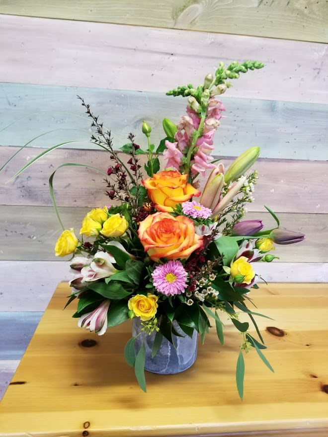 Mixed bouquet in a gray vase with orange roses, yellow spray roses, and pink blooms