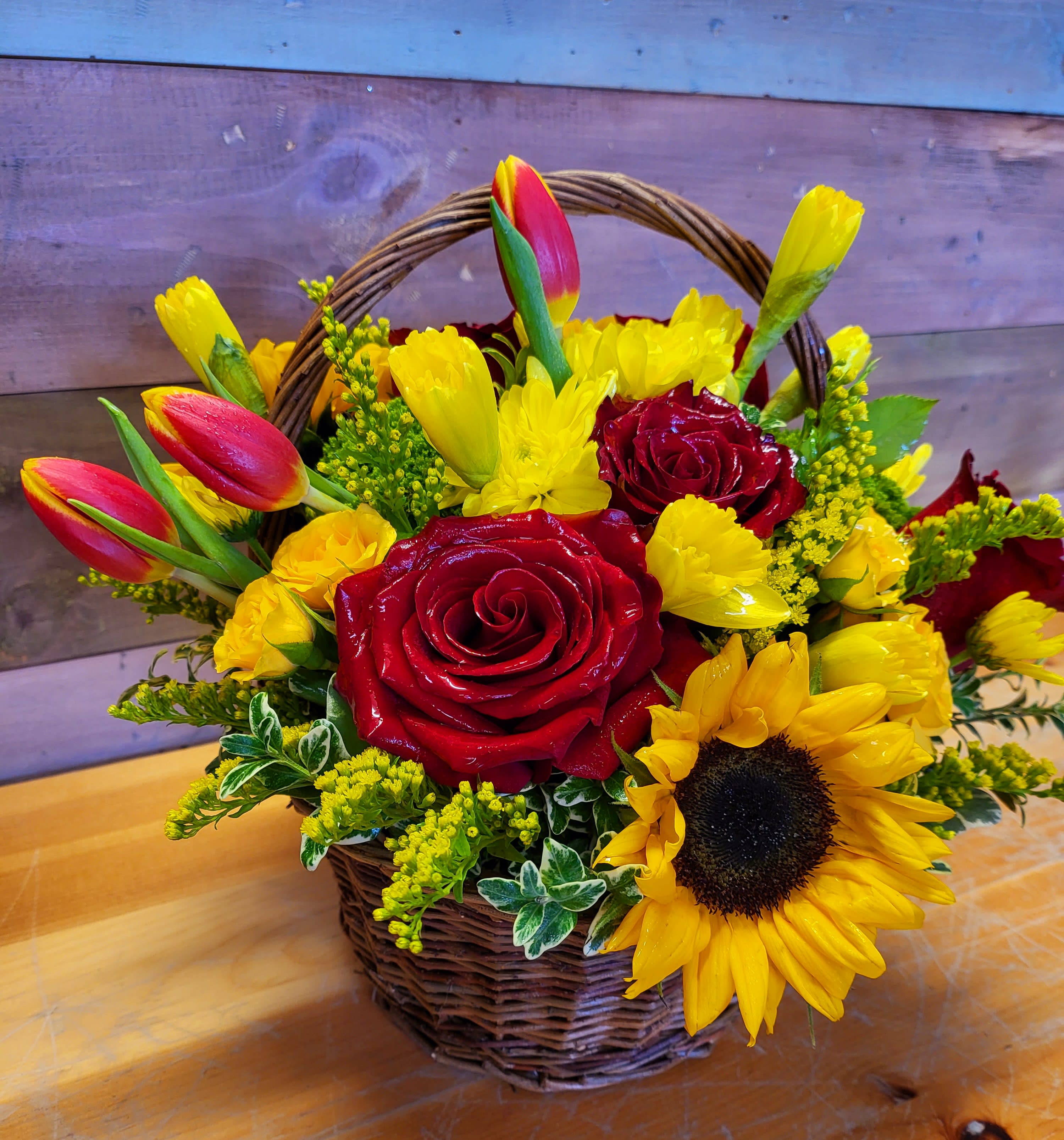 Basket arrangement with red roses, yellow tulips, and a sunflower