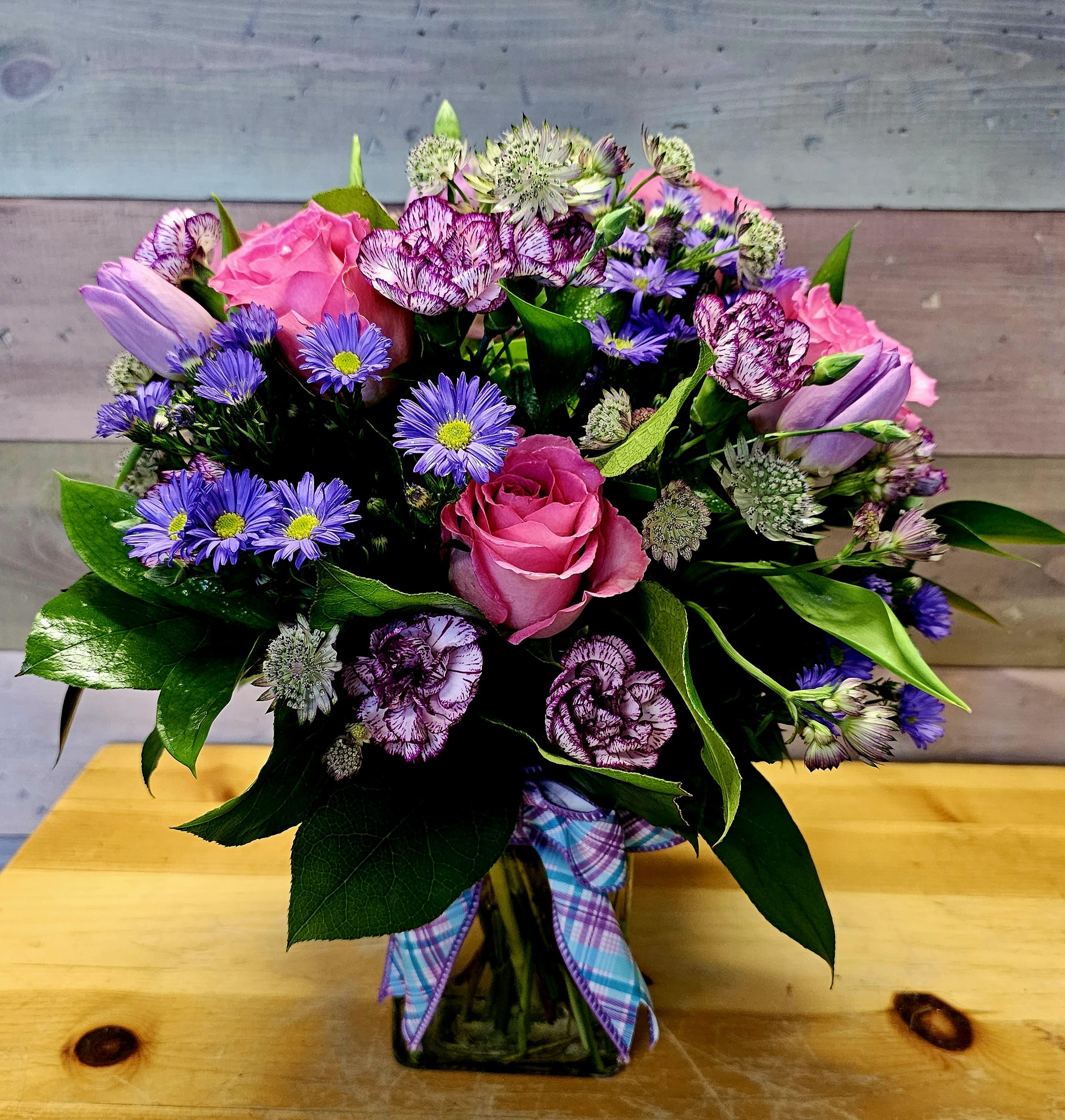 Bouquet of pink roses, purple daisies, and carnations in a glass vase