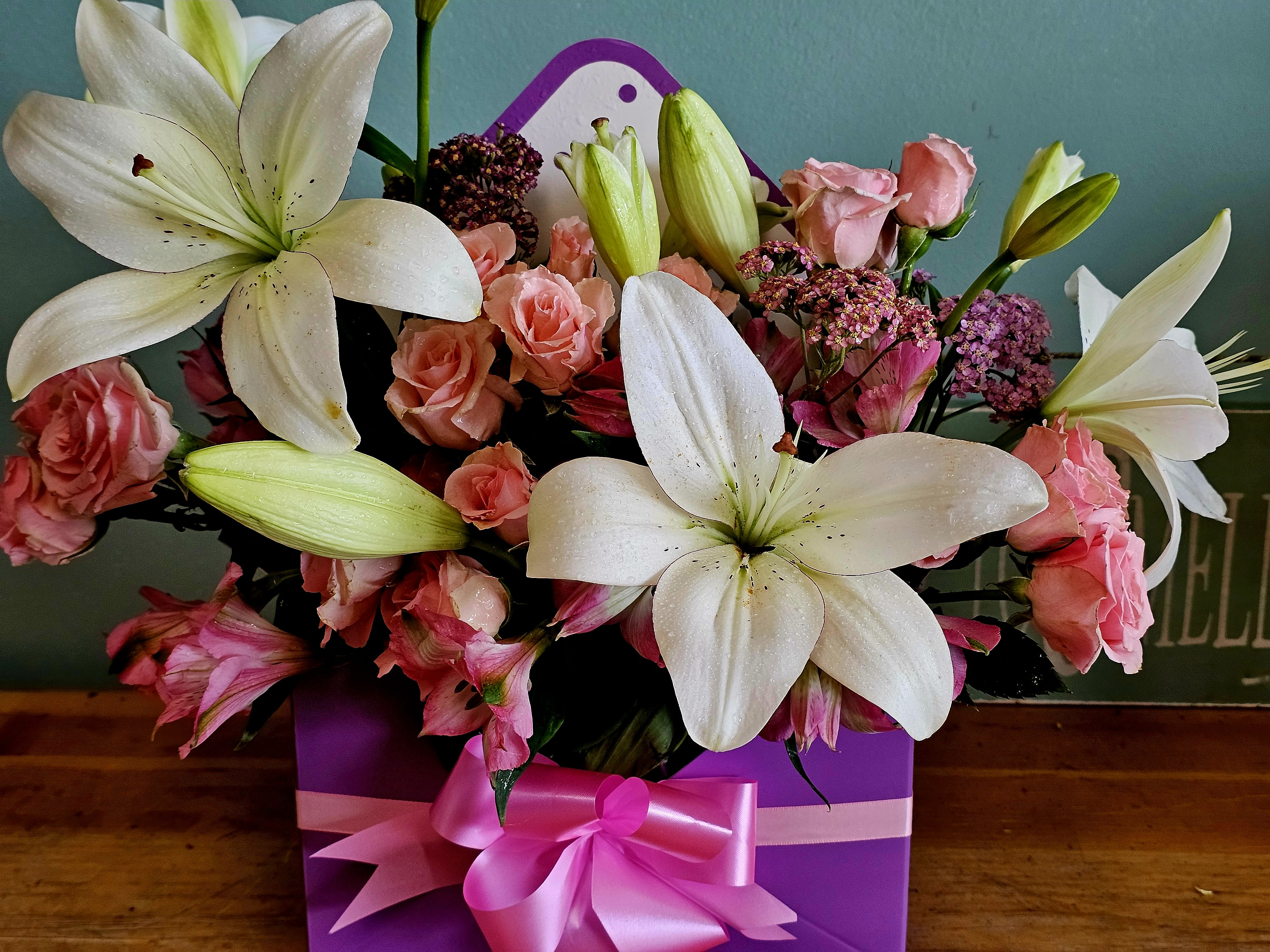 Pink roses and white lilies arranged in a purple gift box with a pink ribbon