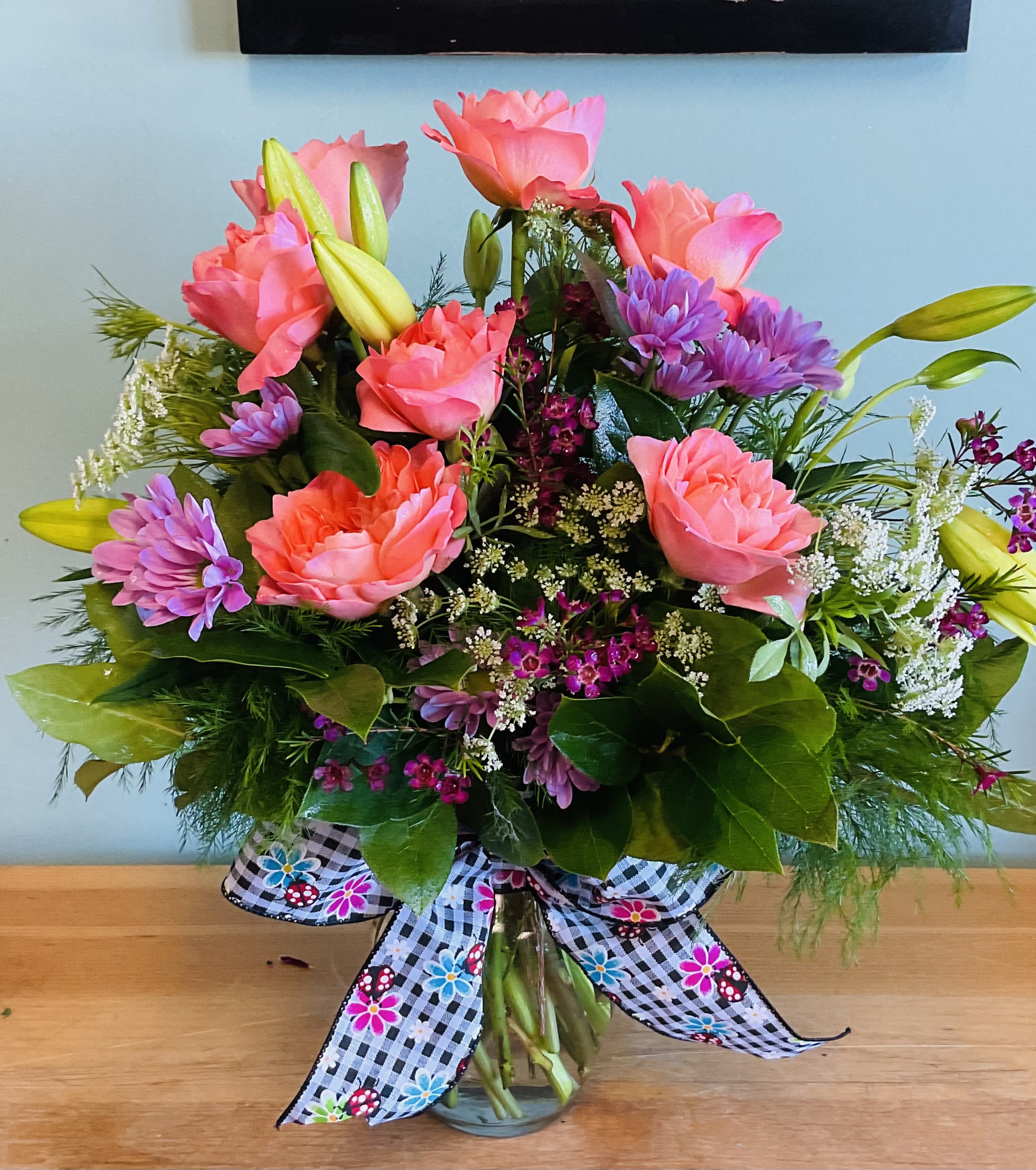 Pink roses and purple daisies in a glass vase with a patterned bow