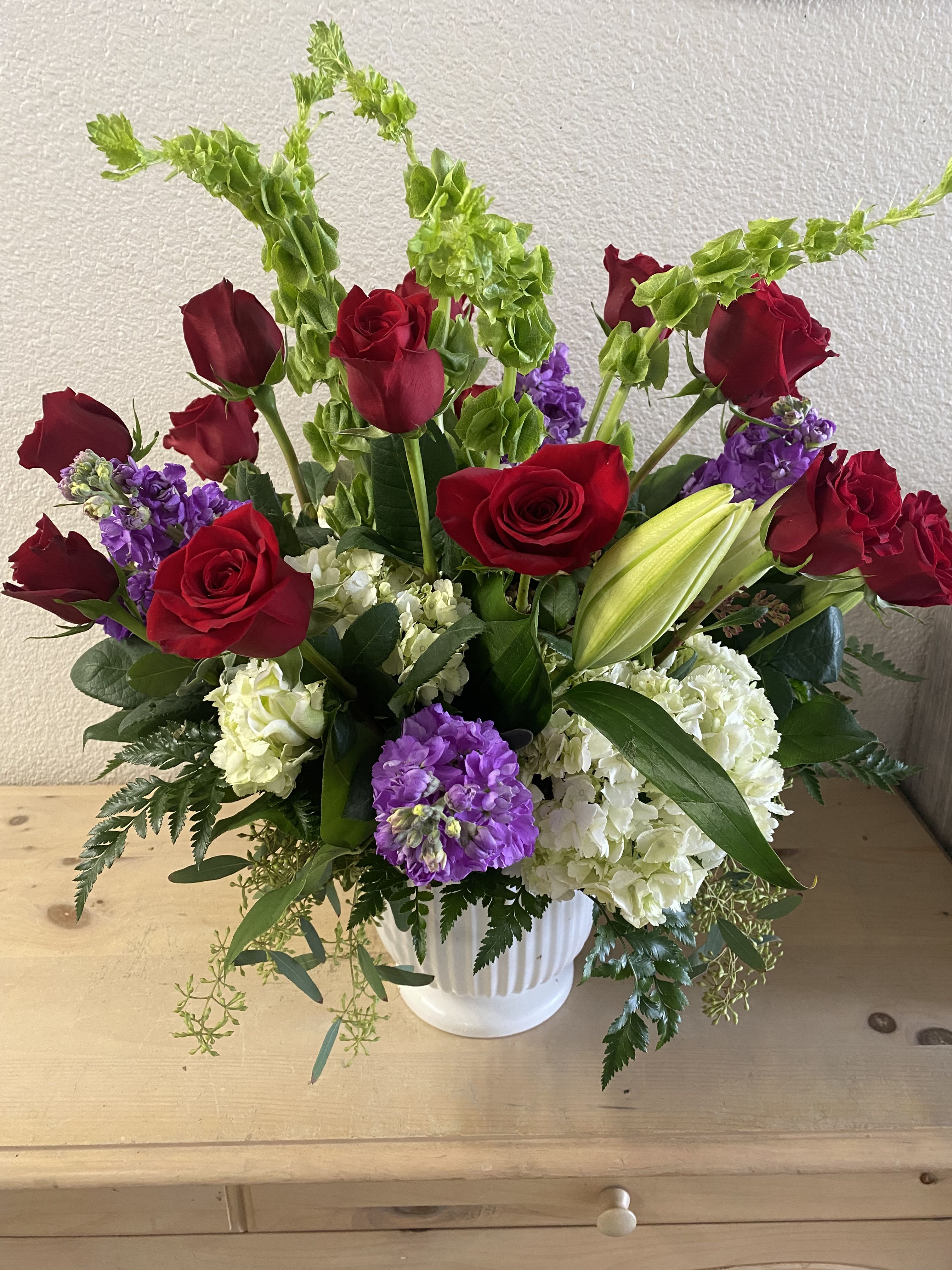 Red roses and purple blooms in a white vase