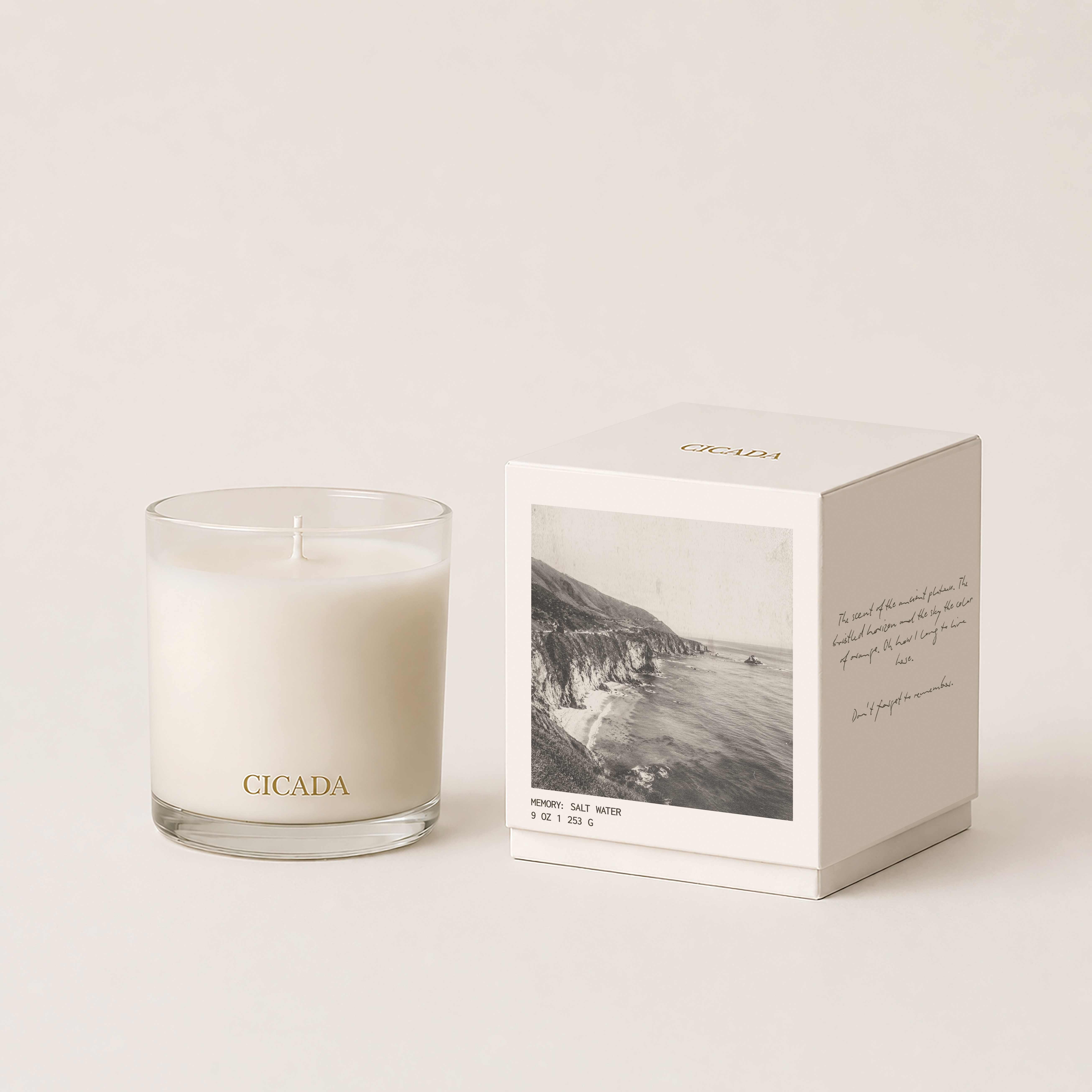 White candle in a glass tumbler beside a boxed candle