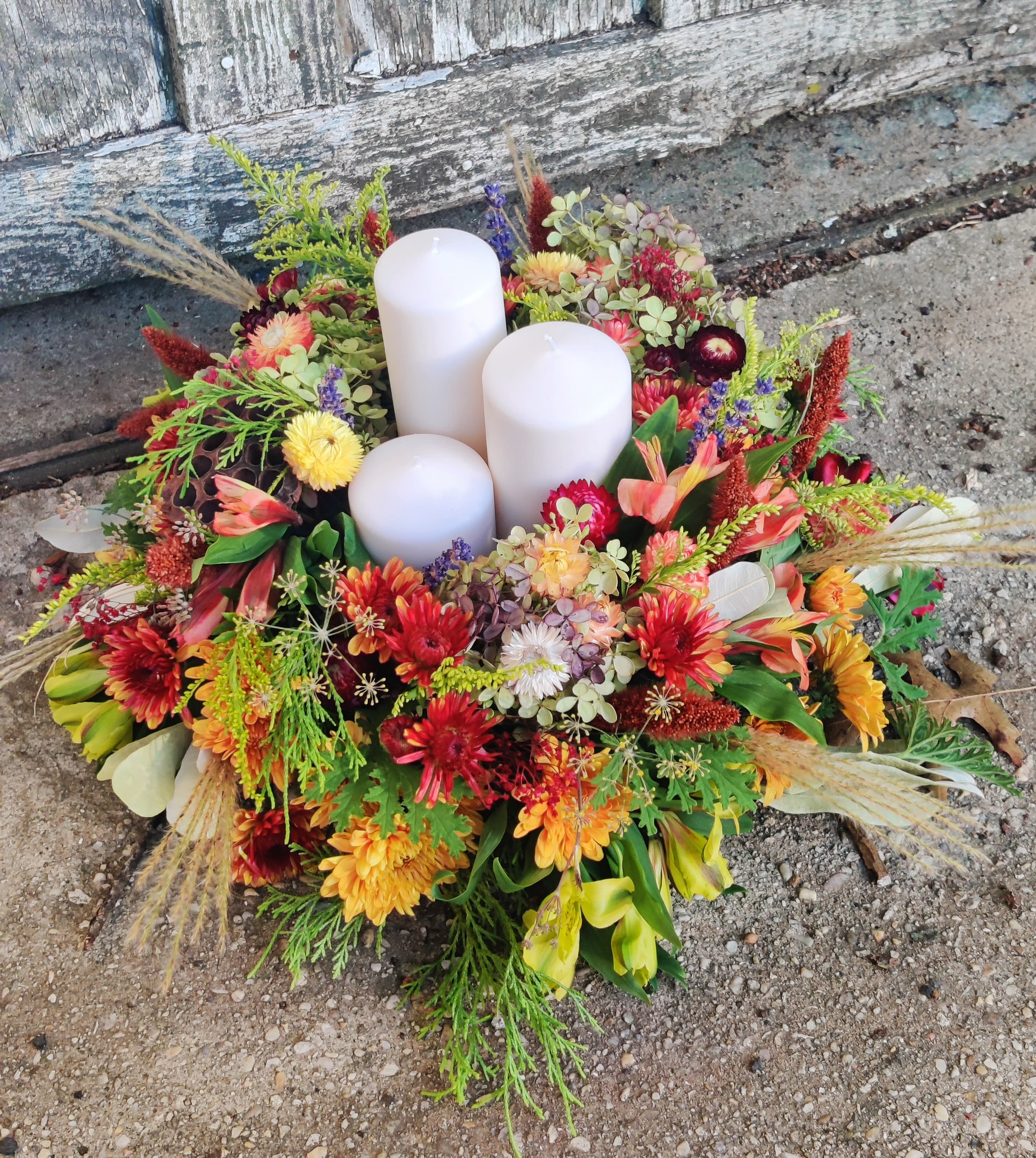 Harvest Arrangement with a Trio of Candles  - Enjoy a mixed arrangement of fall flowers and foliage with dried flowers mixed in; surrounding a trio of candles. Makes a heart warming gift. 
