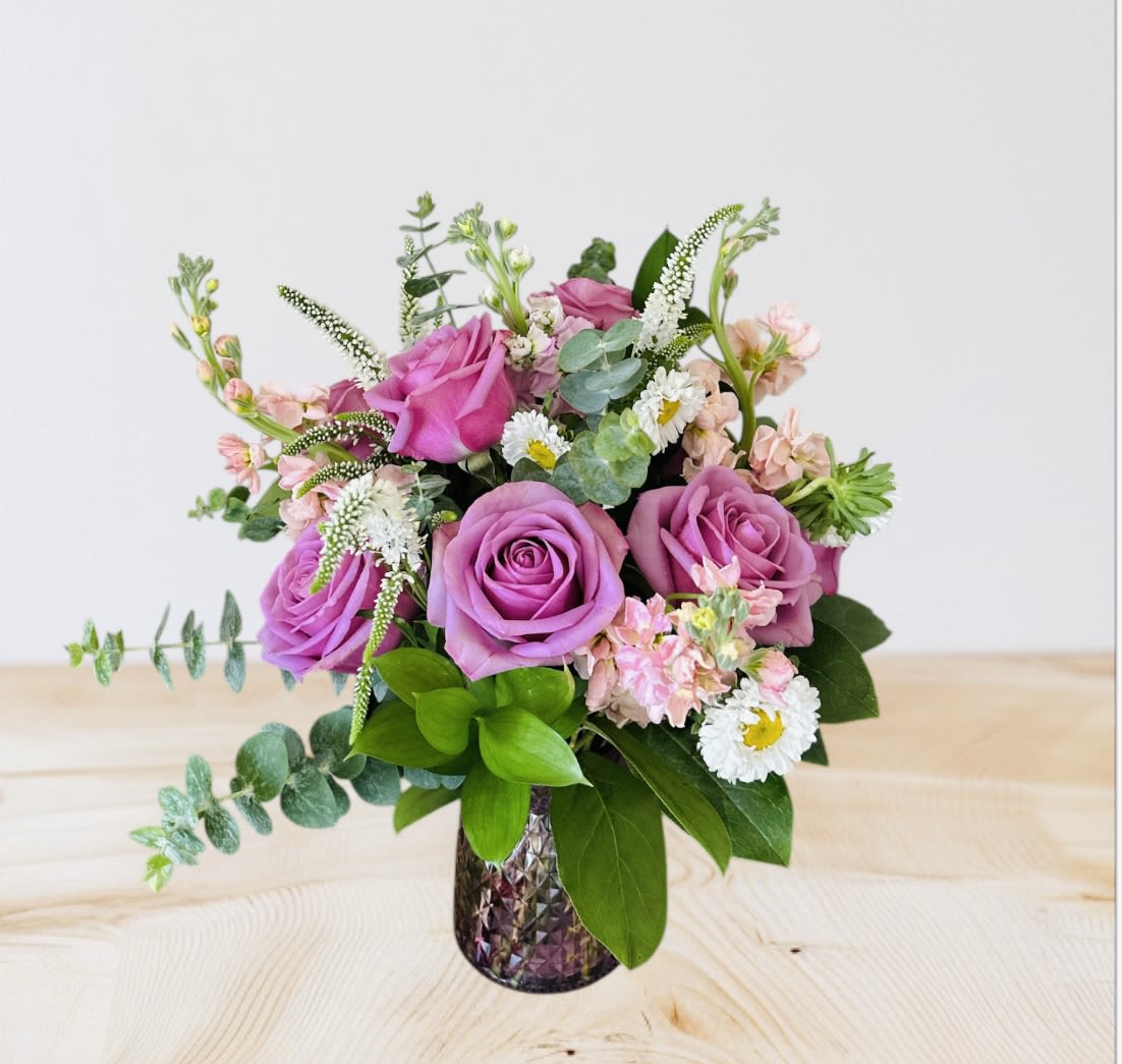 Pink and lavender roses arranged in a textured glass vase with small white and pink accent flowers.