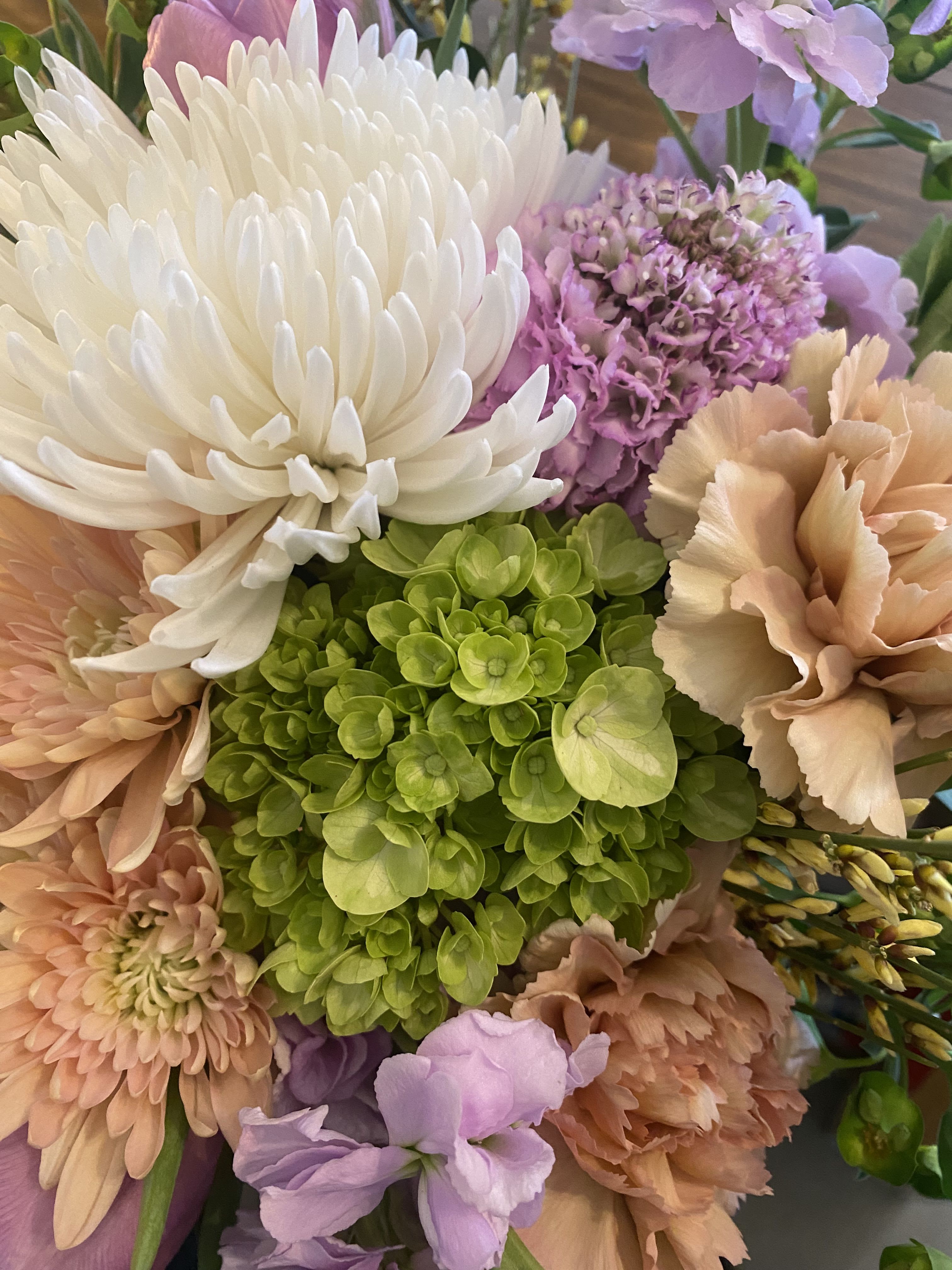 Close-up bouquet of white, peach, and lavender flowers with a green hydrangea center