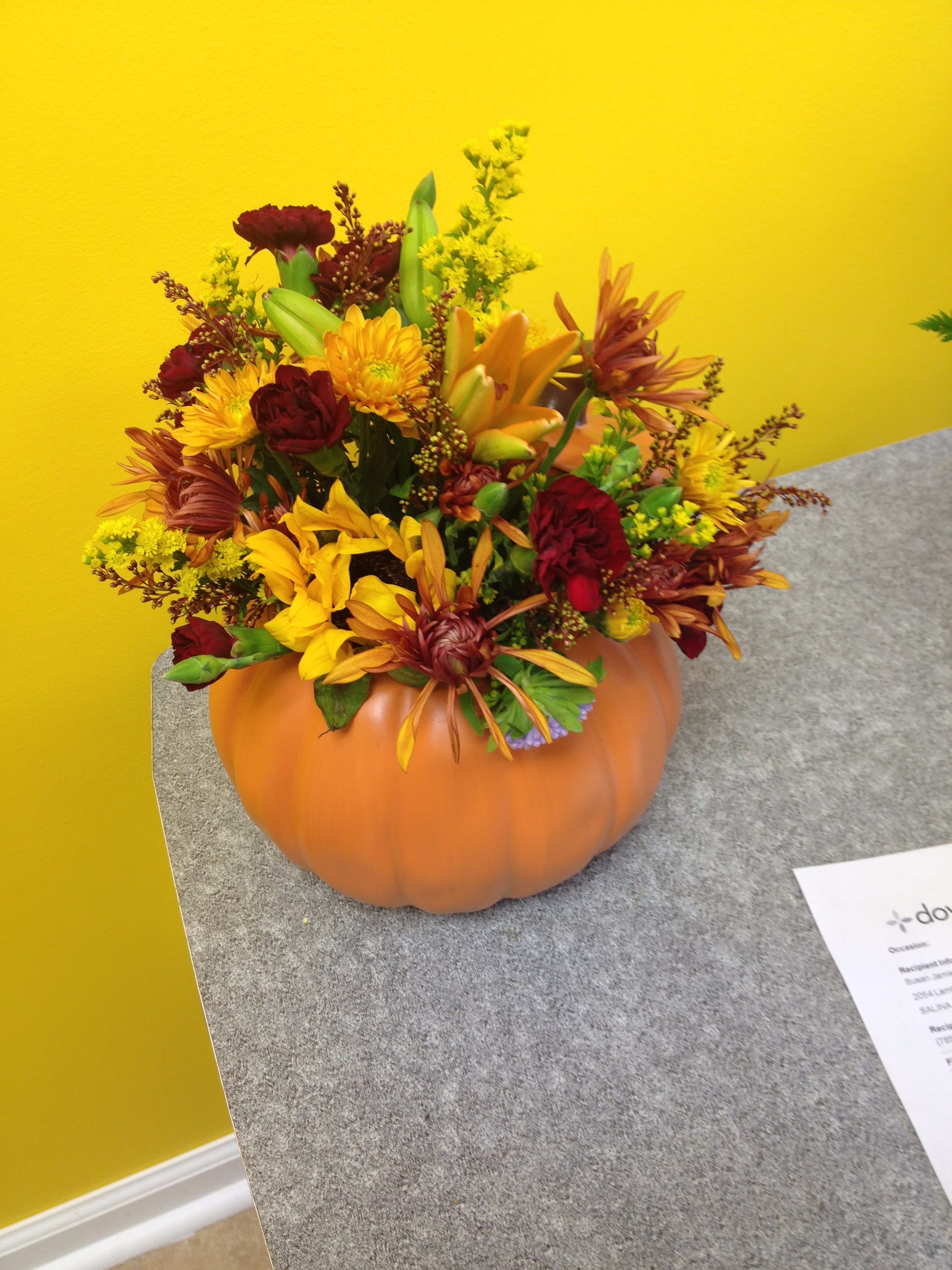 Autumn flower arrangement in a pumpkin container with yellow and burgundy blooms