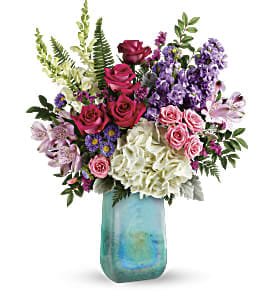 Mixed bouquet of roses, hydrangeas, and purple flowers in a blue glass vase