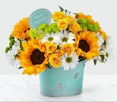 Sunflowers, yellow roses, and white daisies in a turquoise container