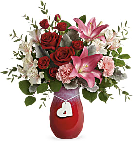 Red roses and pink lilies in a red vase with a heart charm