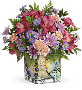 Mixed bouquet of pink, purple, and peach flowers in a decorative square vase