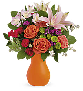 Mixed bouquet of pink lilies, roses, and carnations in an orange vase