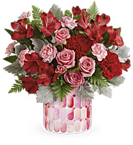 Red and pink flower arrangement in a patterned glass vase