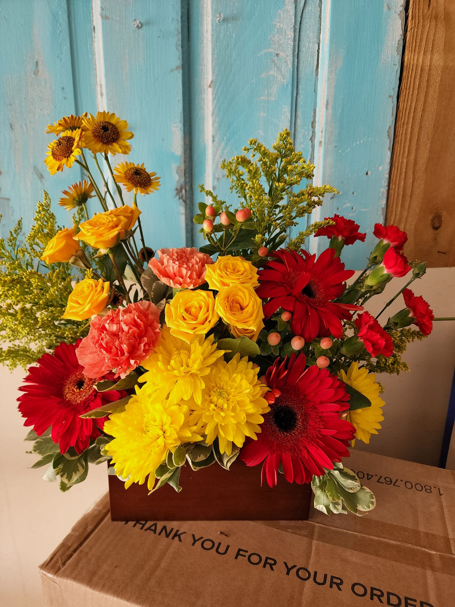 Bright mixed bouquet with red gerberas, yellow roses, and carnations in a box