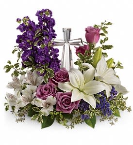 Purple and white floral arrangement with roses and lilies around a silver cross