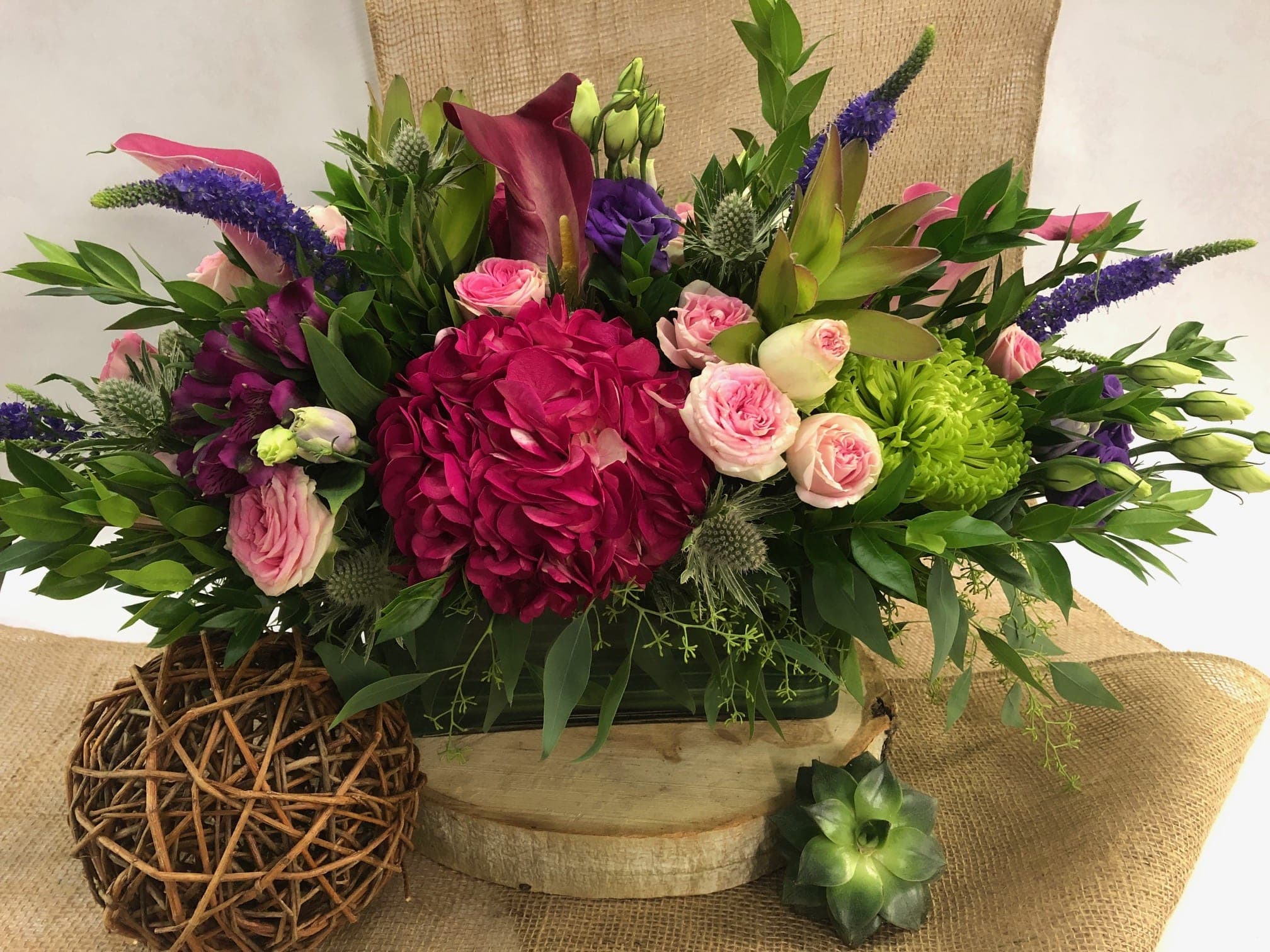 Mixed floral arrangement with pink roses, magenta hydrangea, and purple spikes in a low container