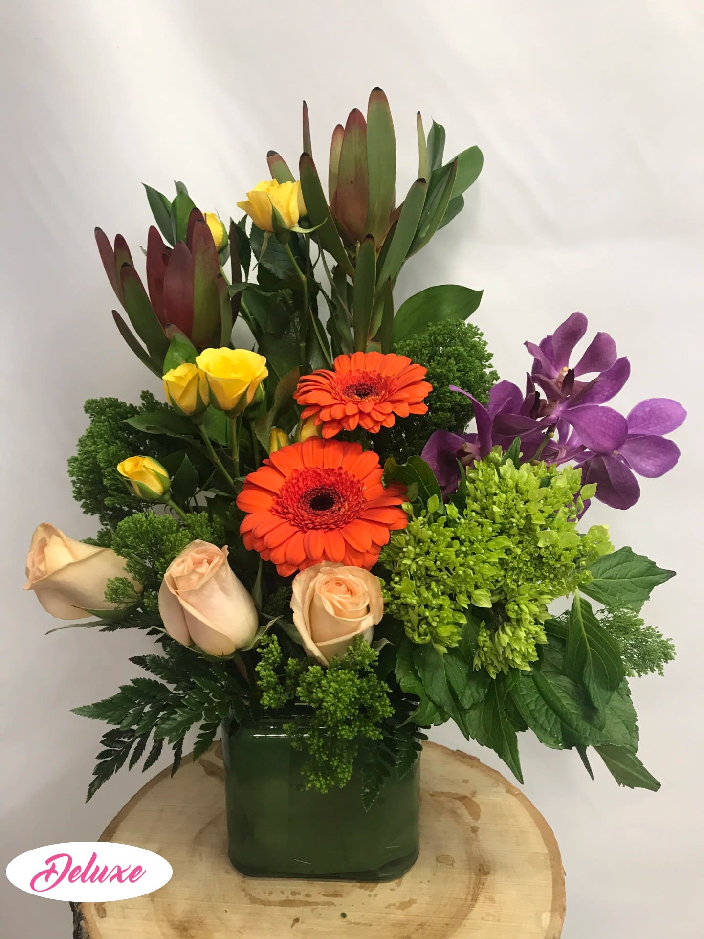 Mixed bouquet in a green vase with orange gerberas, roses, and purple orchids