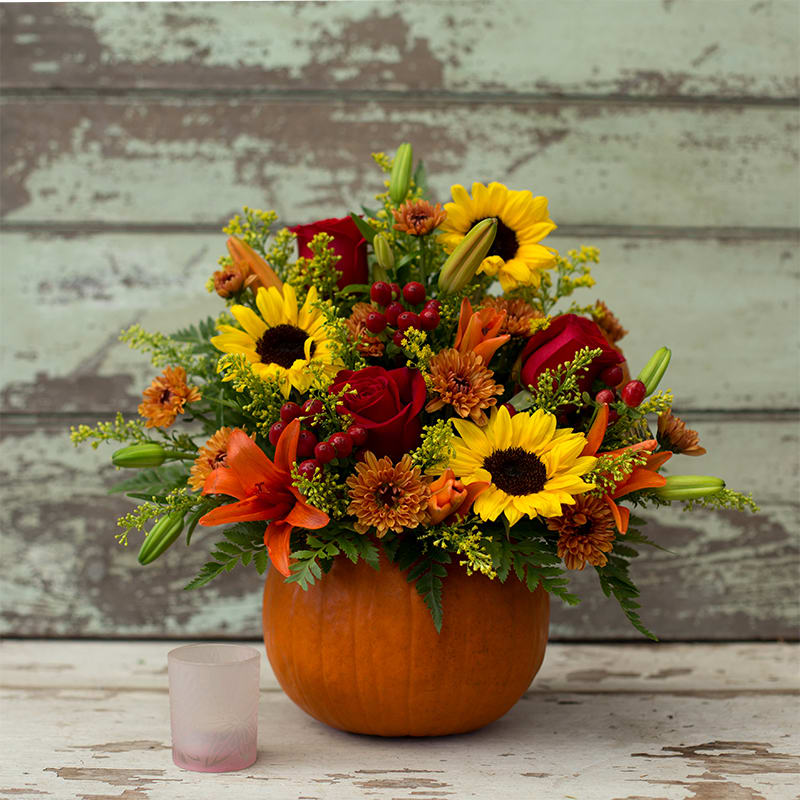 Autumn bouquet in a pumpkin container with sunflowers, roses, lilies, and mums