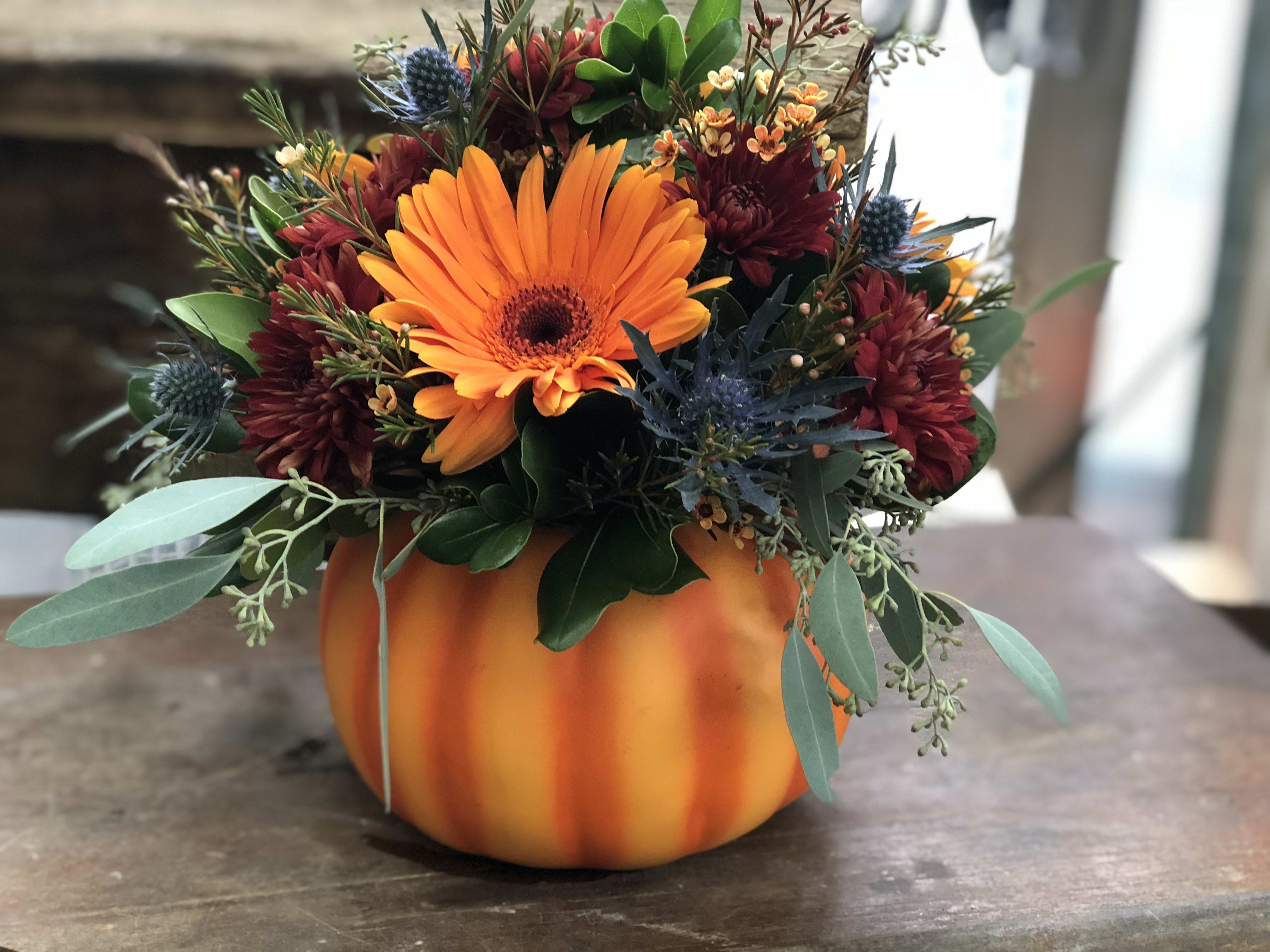 Orange and burgundy floral arrangement in a pumpkin-shaped container