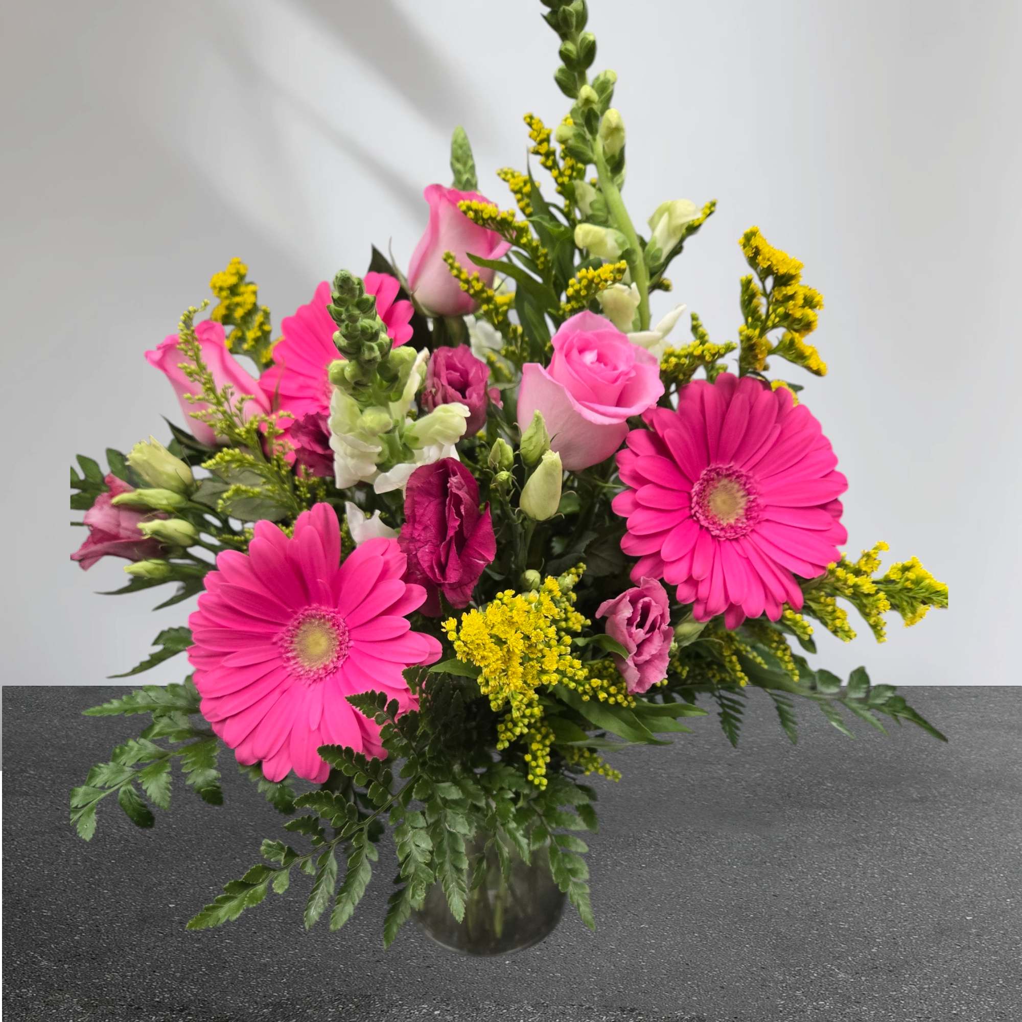 Pink gerberas and roses in a glass vase with yellow filler flowers