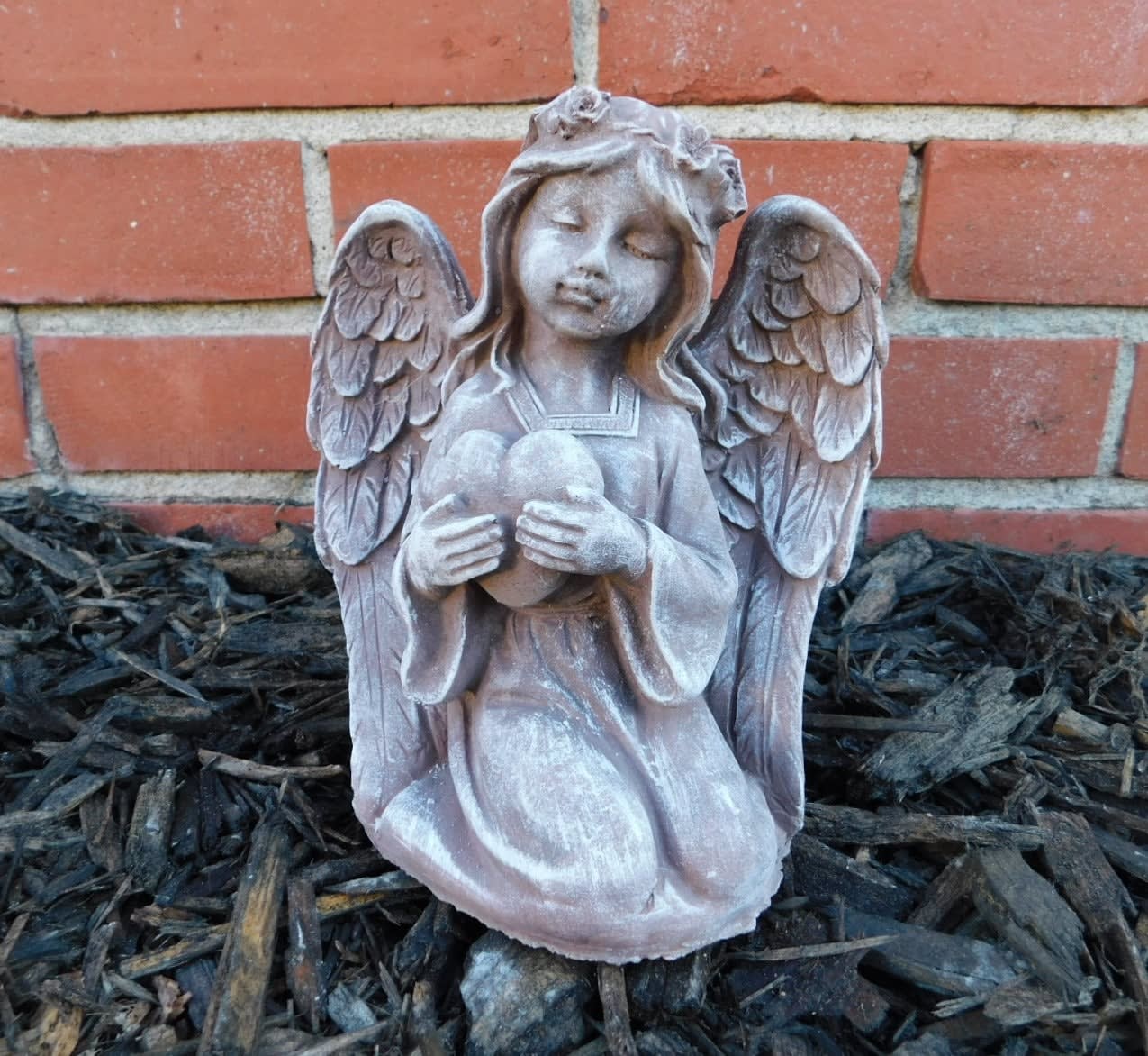 Stone angel figurine holding a heart in front of a brick wall