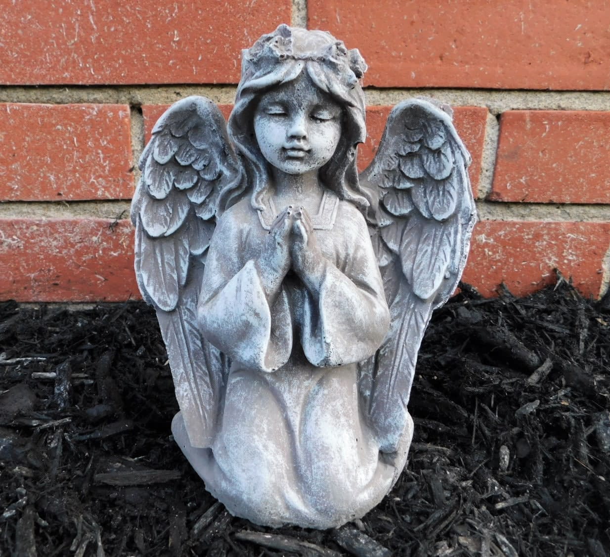 Stone angel statue kneeling with folded hands against a brick wall