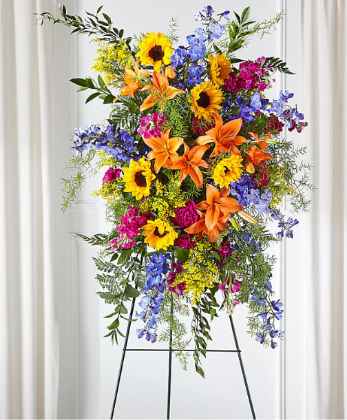 Sunlit Memories Standing - Our Sunlit Memories Standing Spray is crafted with a mix of fuchsia, deep blue, hot pink and orange florals to celebrate their radiant life. This vibrant display combines bright shades with stunning texture while sharing thoughtful sentiments and comfort to loved ones.  Please Note: The bouquet pictured reflects our original design for this product. While we always try to follow the color palette, we may replace stems to deliver the freshest bouquet possible. 